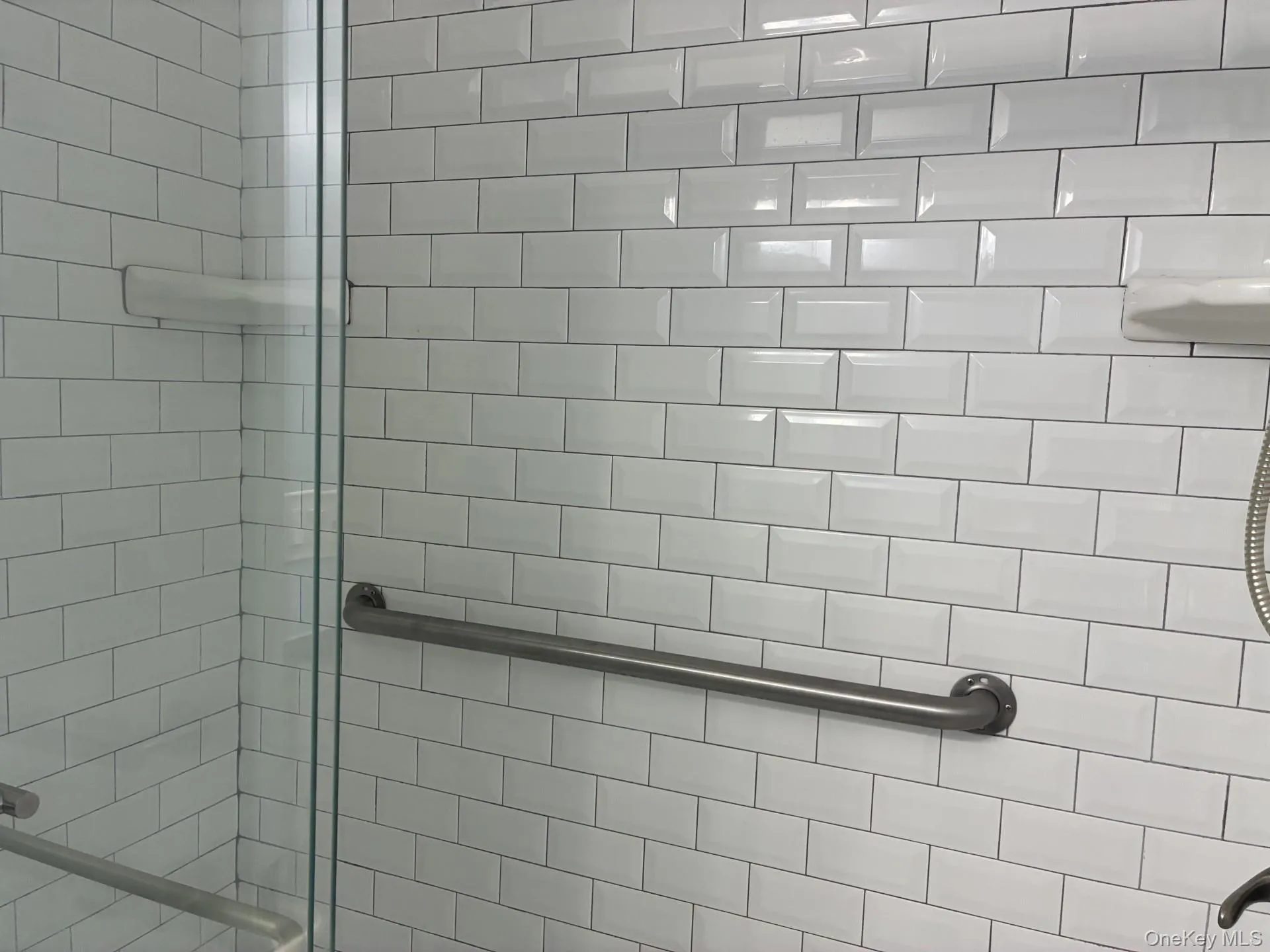 Shower enclosure featuring white subway tile, a chrome grab bar, and clear glass panels Shower enclosure featuring white subway tile, a chrome grab bar, and clear glass panels