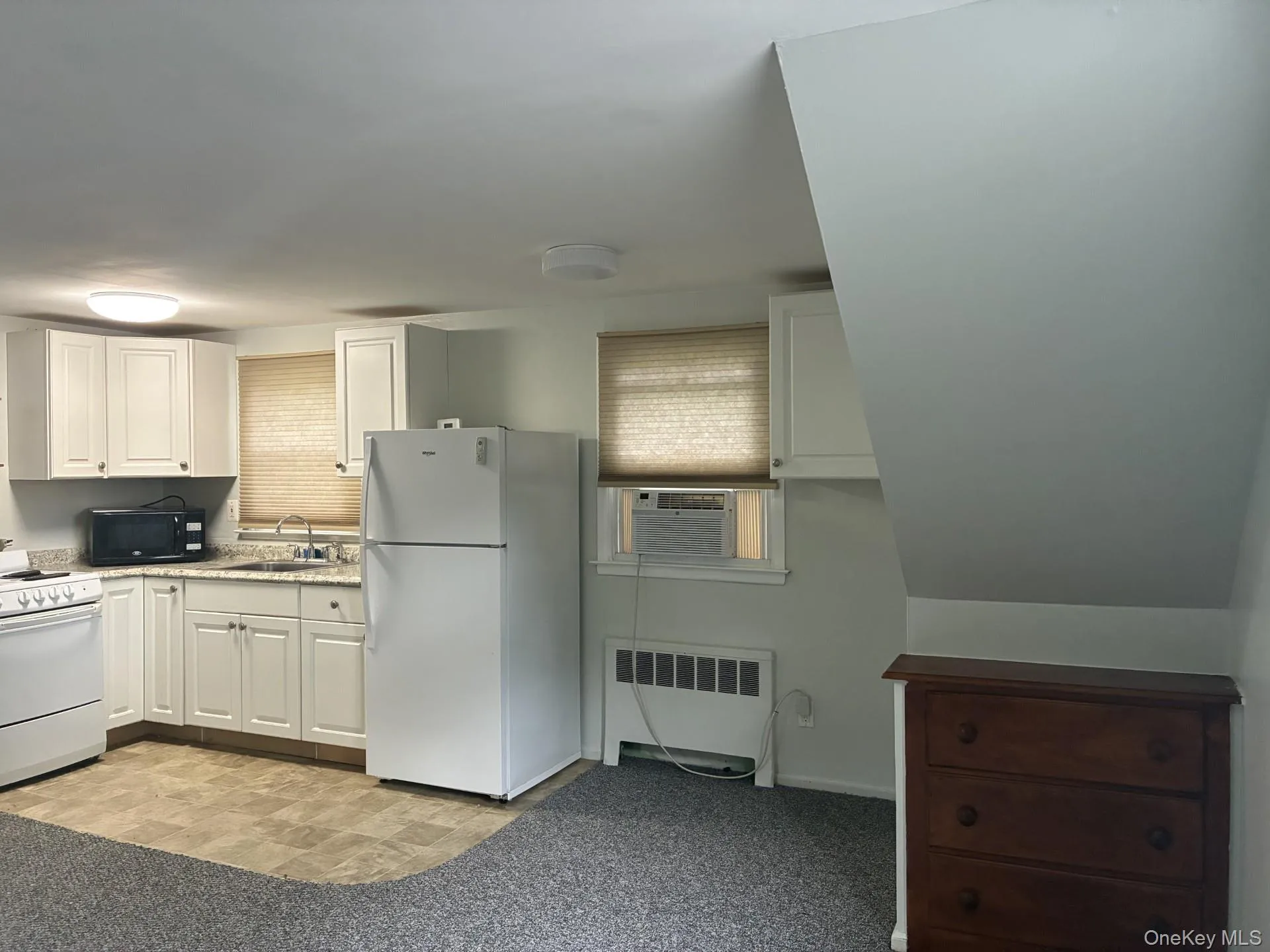 White kitchen cabinetry with a corner sink, light-colored countertops, and white appliances White kitchen cabinetry with a corner sink, light-colored countertops, and white appliances