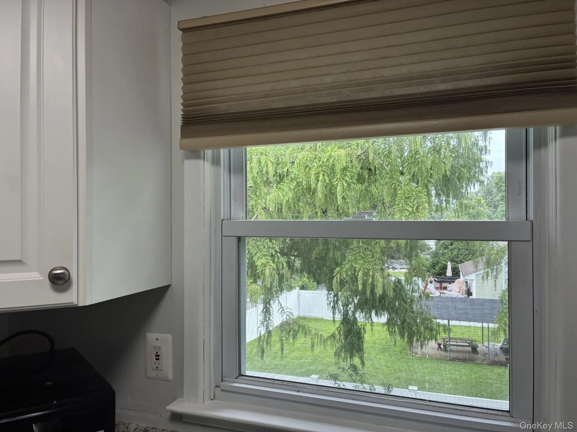 White framed window overlooking a green yard, featuring a pleated window shade and white cabinetry White framed window overlooking a green yard, featuring a pleated window shade and white cabinetry