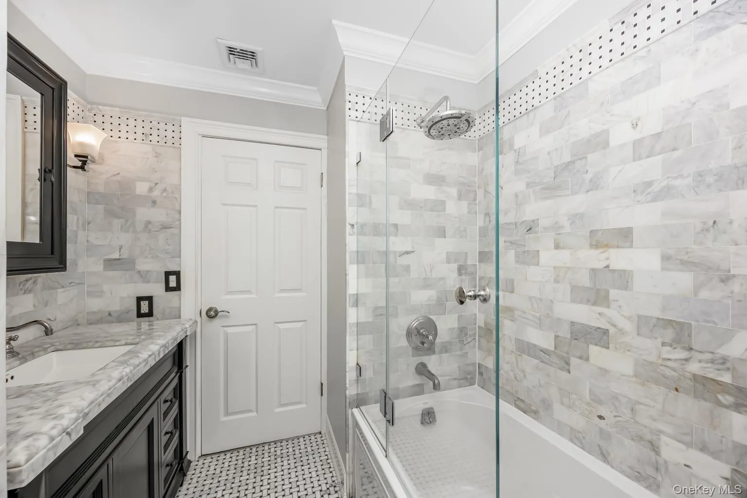White subway tile shower surround with a rain shower head, glass shower enclosure, white bathtub, and mosaic tile flooring White subway tile shower surround with a rain shower head, glass shower enclosure, white bathtub, and mosaic tile flooring