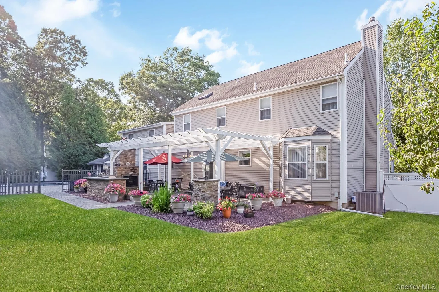 Expansive backyard featuring a manicured lawn, a stone patio with a white pergola, and an outdoor kitchen area with a built-in grill Expansive backyard featuring a manicured lawn, a stone patio with a white pergola, and an outdoor kitchen area with a built-in grill