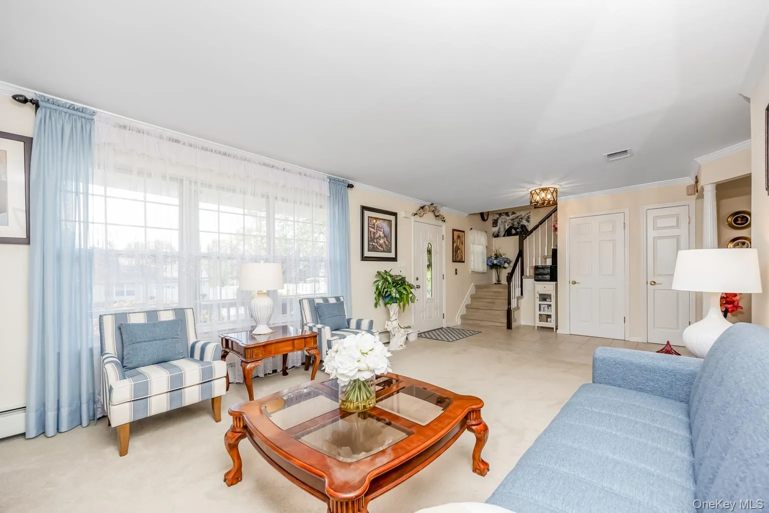 Spacious living area featuring expansive windows, neutral carpeting, and a staircase with dark wood handrail Spacious living area featuring expansive windows, neutral carpeting, and a staircase with dark wood handrail