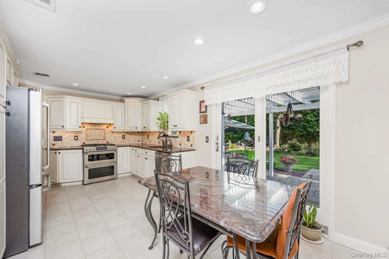 Kitchen featuring white cabinetry, stainless steel appliances, dark countertops, and a tiled backsplash, with sliding glass doors opening to the exterior Kitchen featuring white cabinetry, stainless steel appliances, dark countertops, and a tiled backsplash, with sliding glass doors opening to the exterior