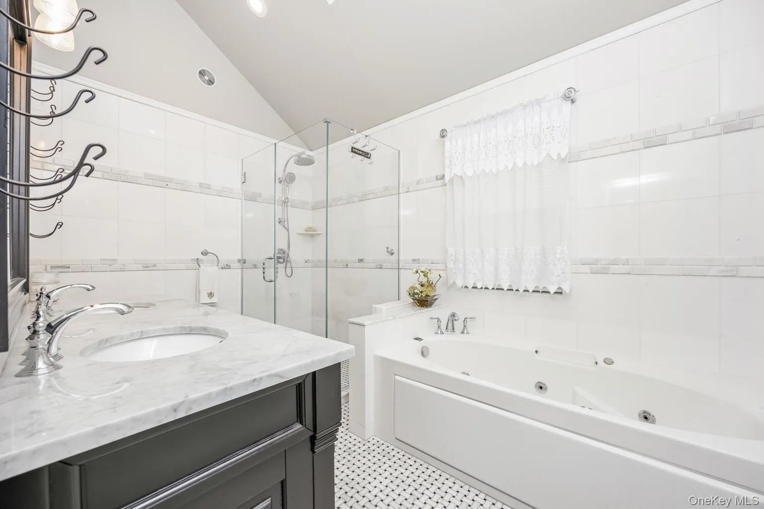 White tiled bathroom featuring a single vanity with stone countertop, glass-enclosed shower, built-in soaking tub, and black and white mosaic flooring White tiled bathroom featuring a single vanity with stone countertop, glass-enclosed shower, built-in soaking tub, and black and white mosaic flooring