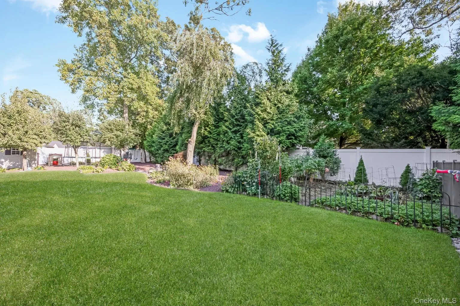 Expansive lawn area with surrounding mature trees, perimeter fencing, and cultivated garden beds Expansive lawn area with surrounding mature trees, perimeter fencing, and cultivated garden beds