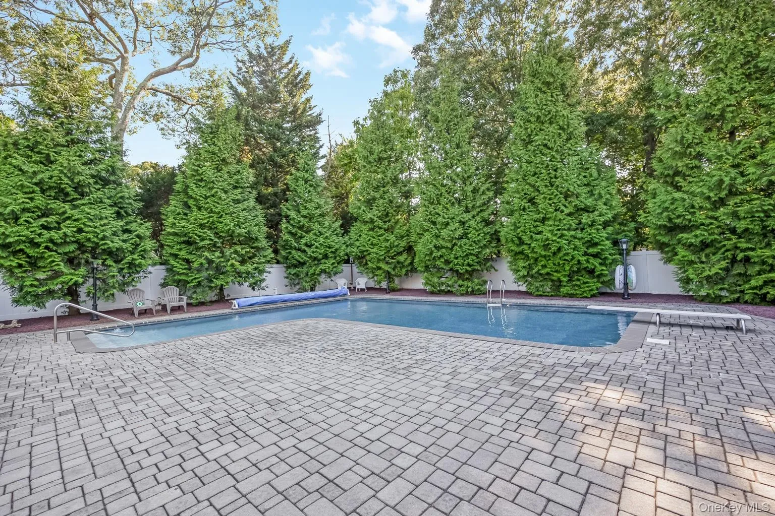 Outdoor swimming pool with integrated steps, surrounded by a paver patio and a privacy fence Outdoor swimming pool with integrated steps, surrounded by a paver patio and a privacy fence