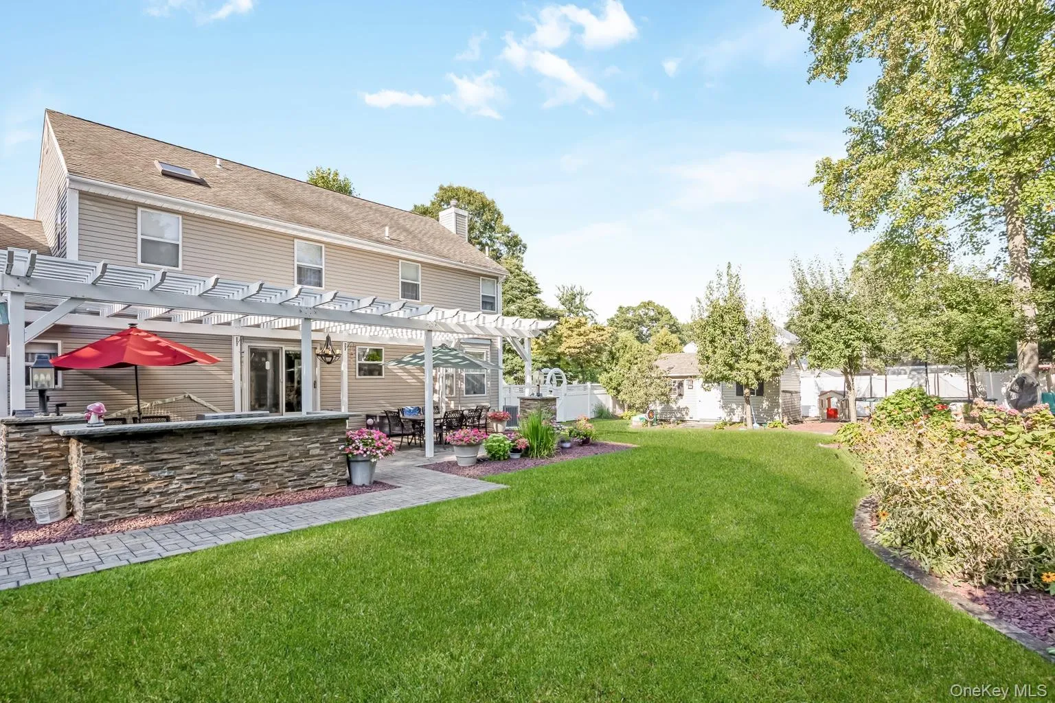 Expansive lawn with a paver patio, stone-faced outdoor kitchen area, and a white pergola structure Expansive lawn with a paver patio, stone-faced outdoor kitchen area, and a white pergola structure