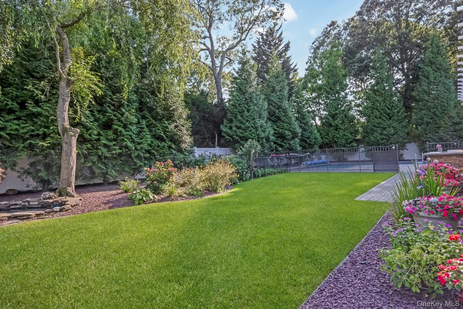 Expansive lawn area with mature perimeter trees, a paved patio, and a fenced-in pool Expansive lawn area with mature perimeter trees, a paved patio, and a fenced-in pool
