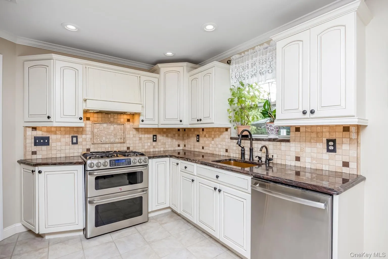 White cabinetry, brown granite countertops, mosaic tile backsplash, stainless steel appliances, and a double oven range White cabinetry, brown granite countertops, mosaic tile backsplash, stainless steel appliances, and a double oven range