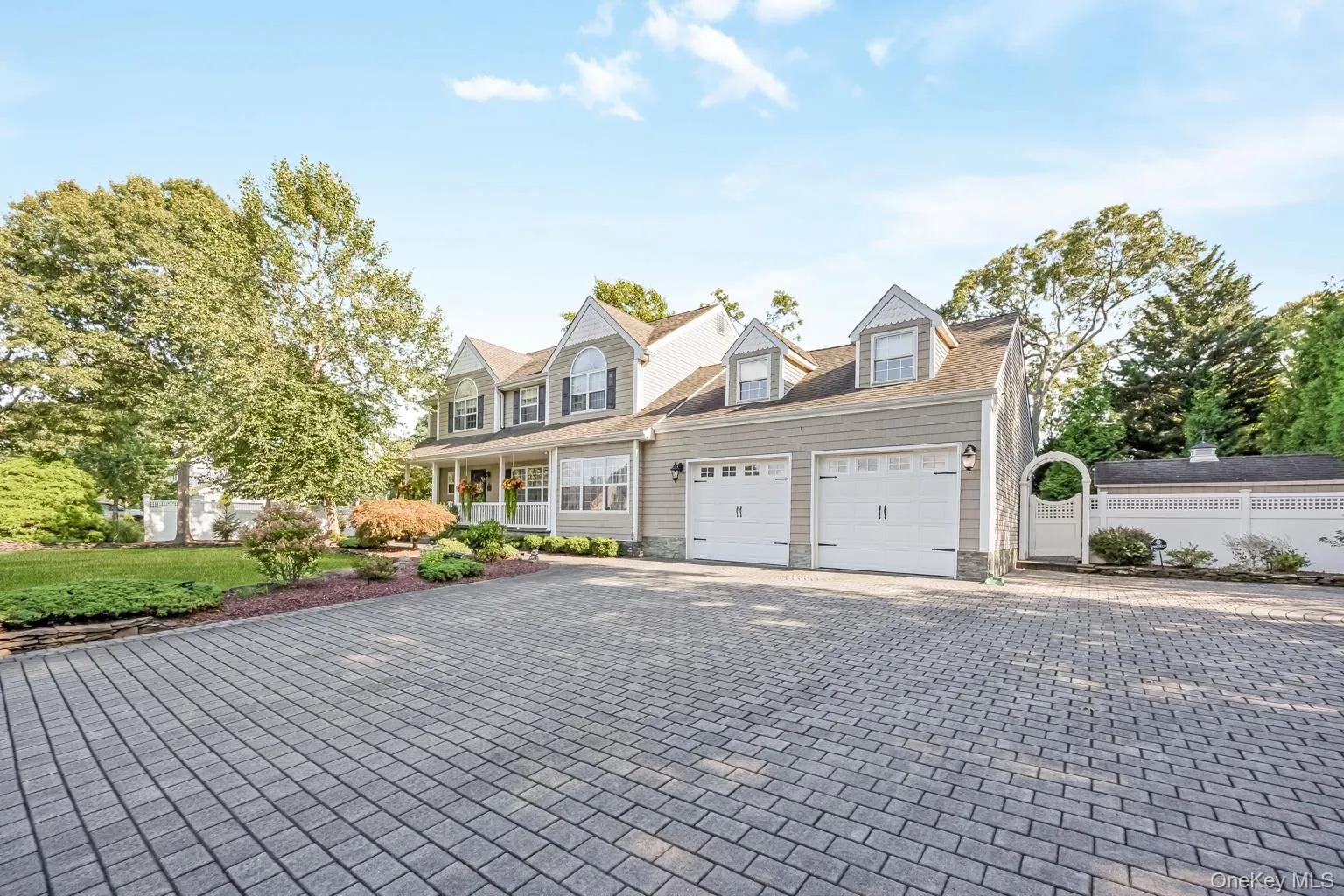 Paved driveway with a two-car garage, dormer windows, covered front porch, and an arched garden gate Paved driveway with a two-car garage, dormer windows, covered front porch, and an arched garden gate