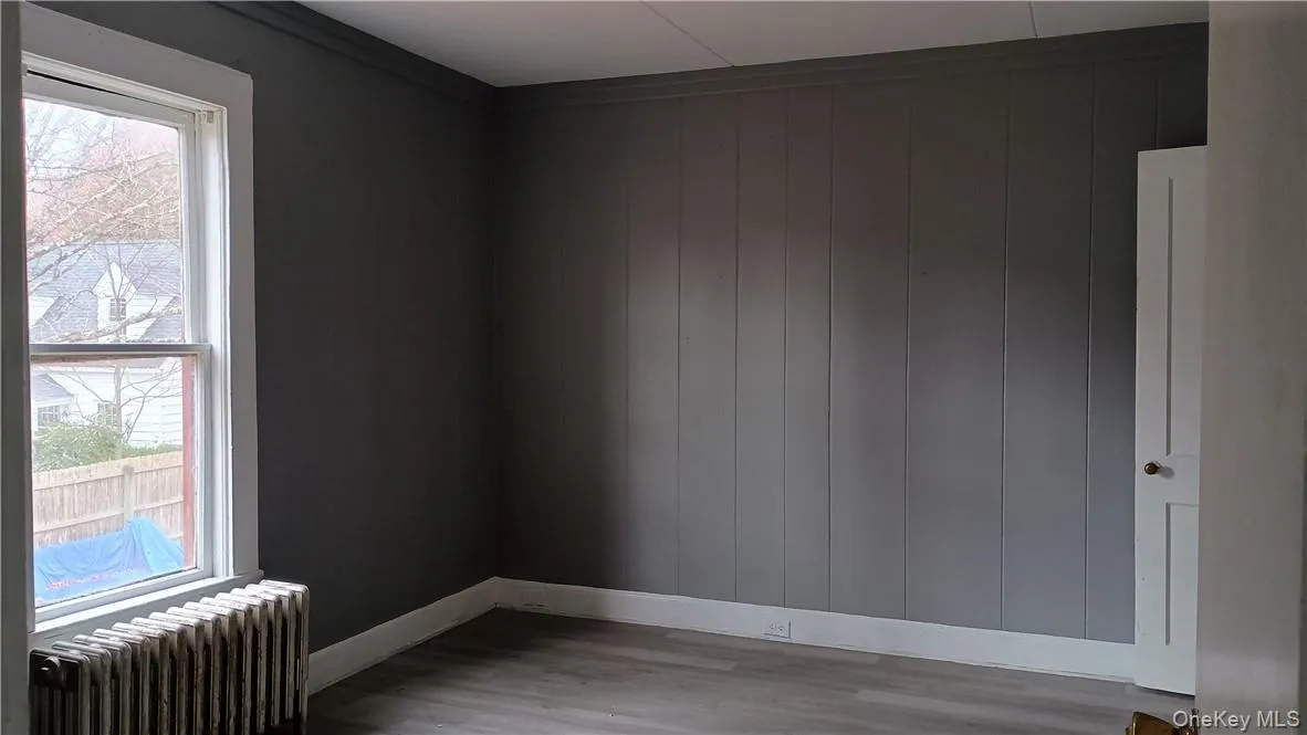 Unfurnished room featuring wood walls, radiator heating unit, wood-type flooring, and ornamental molding Unfurnished room featuring wood walls, radiator heating unit, wood-type flooring, and ornamental molding