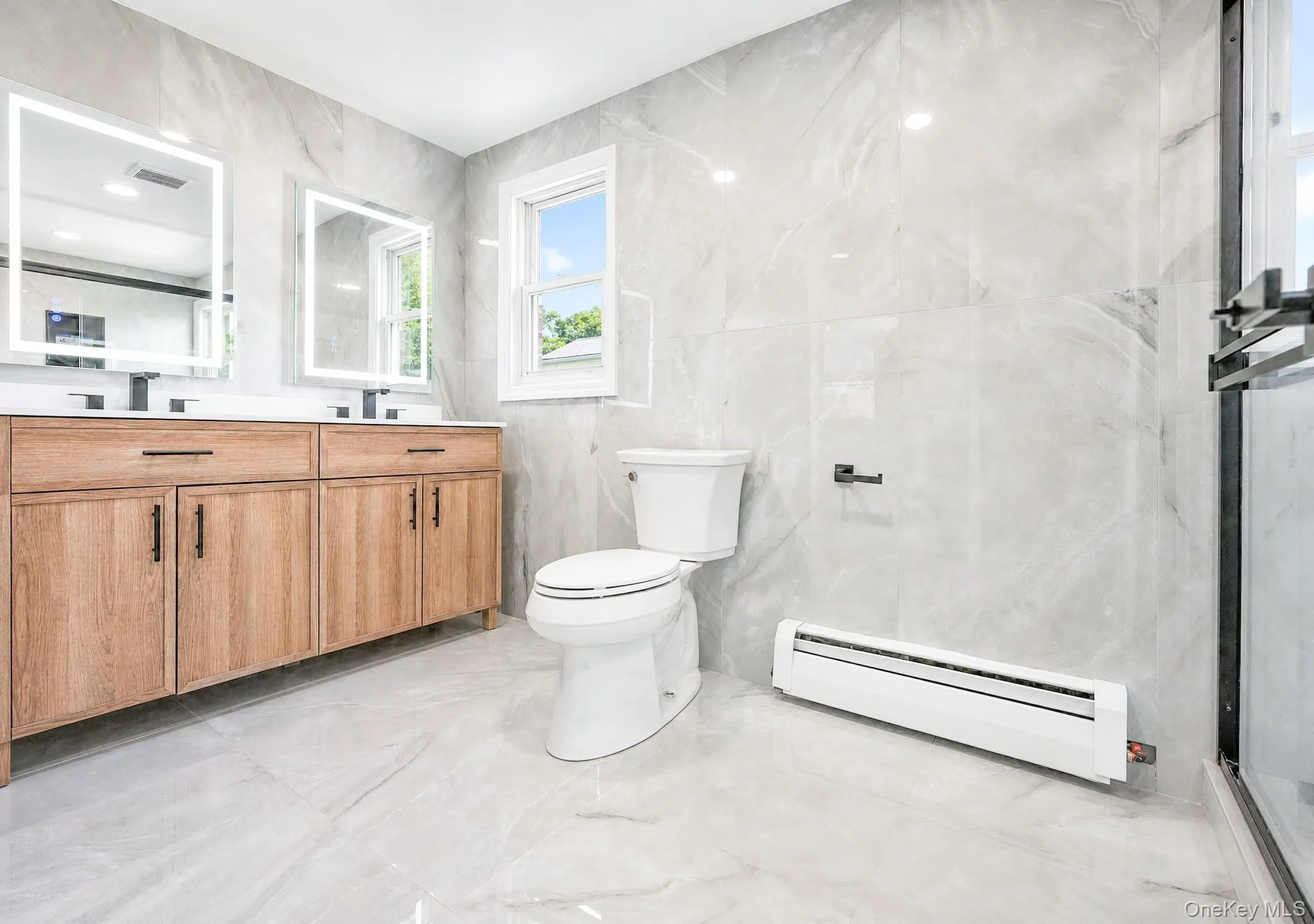 Bathroom featuring a double vanity with wood-finish cabinetry and rectangular illuminated mirrors Bathroom featuring a double vanity with wood-finish cabinetry and rectangular illuminated mirrors