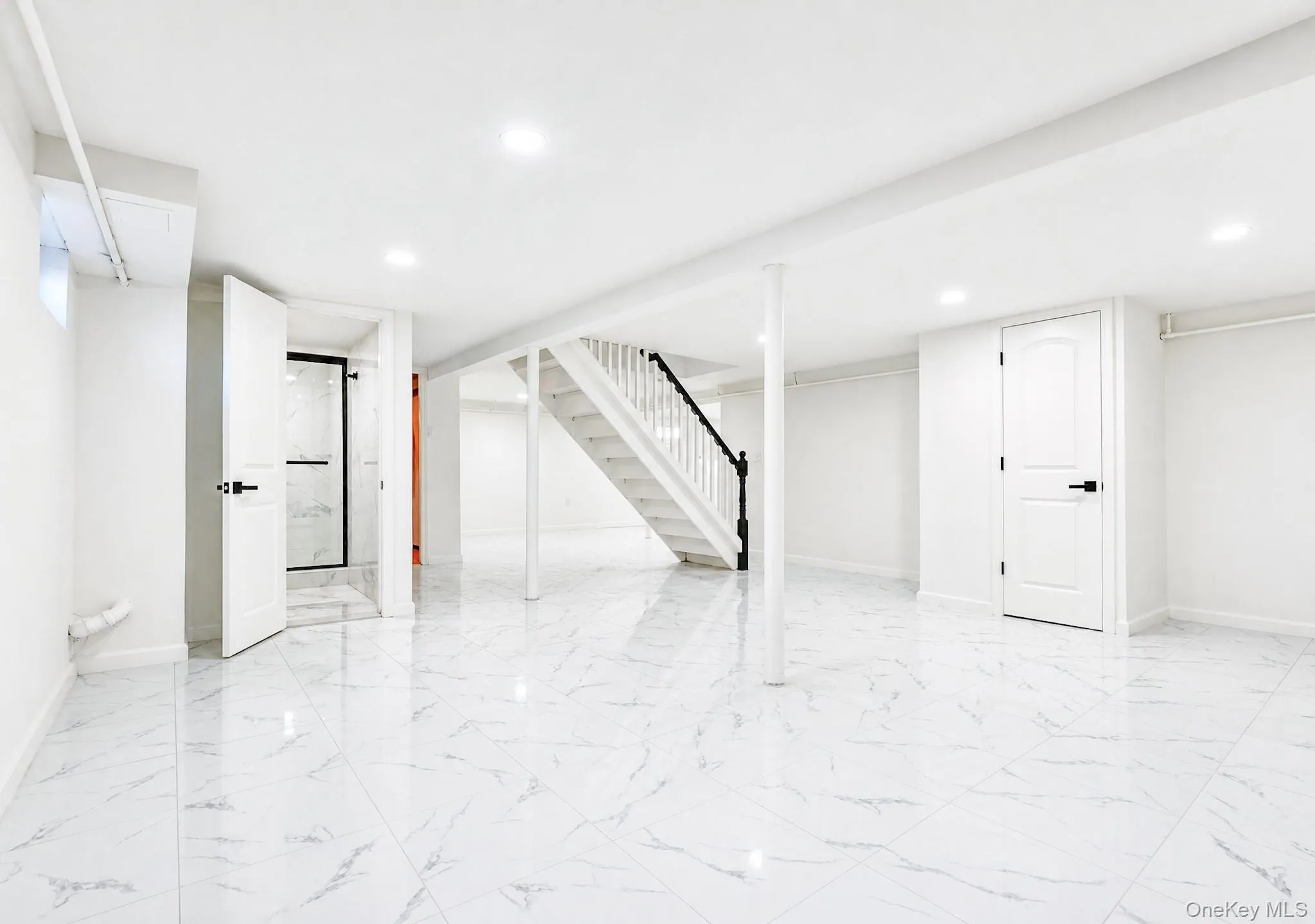 Spacious lower-level area featuring white porcelain tile flooring, recessed lighting, and a white painted staircase with a black handrail Spacious lower-level area featuring white porcelain tile flooring, recessed lighting, and a white painted staircase with a black handrail