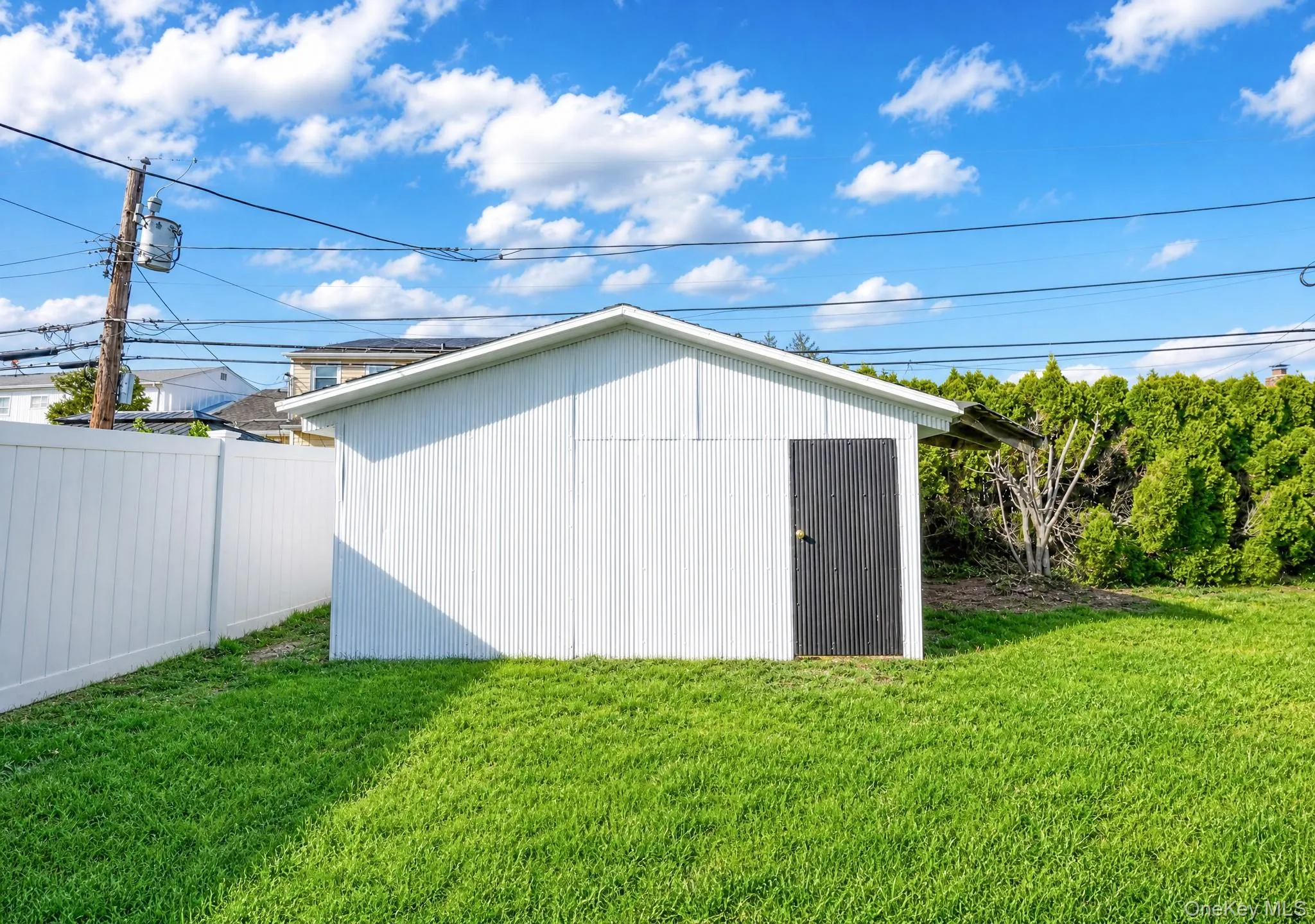 White corrugated metal shed with a dark panel door, set within a vibrant green lawn White corrugated metal shed with a dark panel door, set within a vibrant green lawn