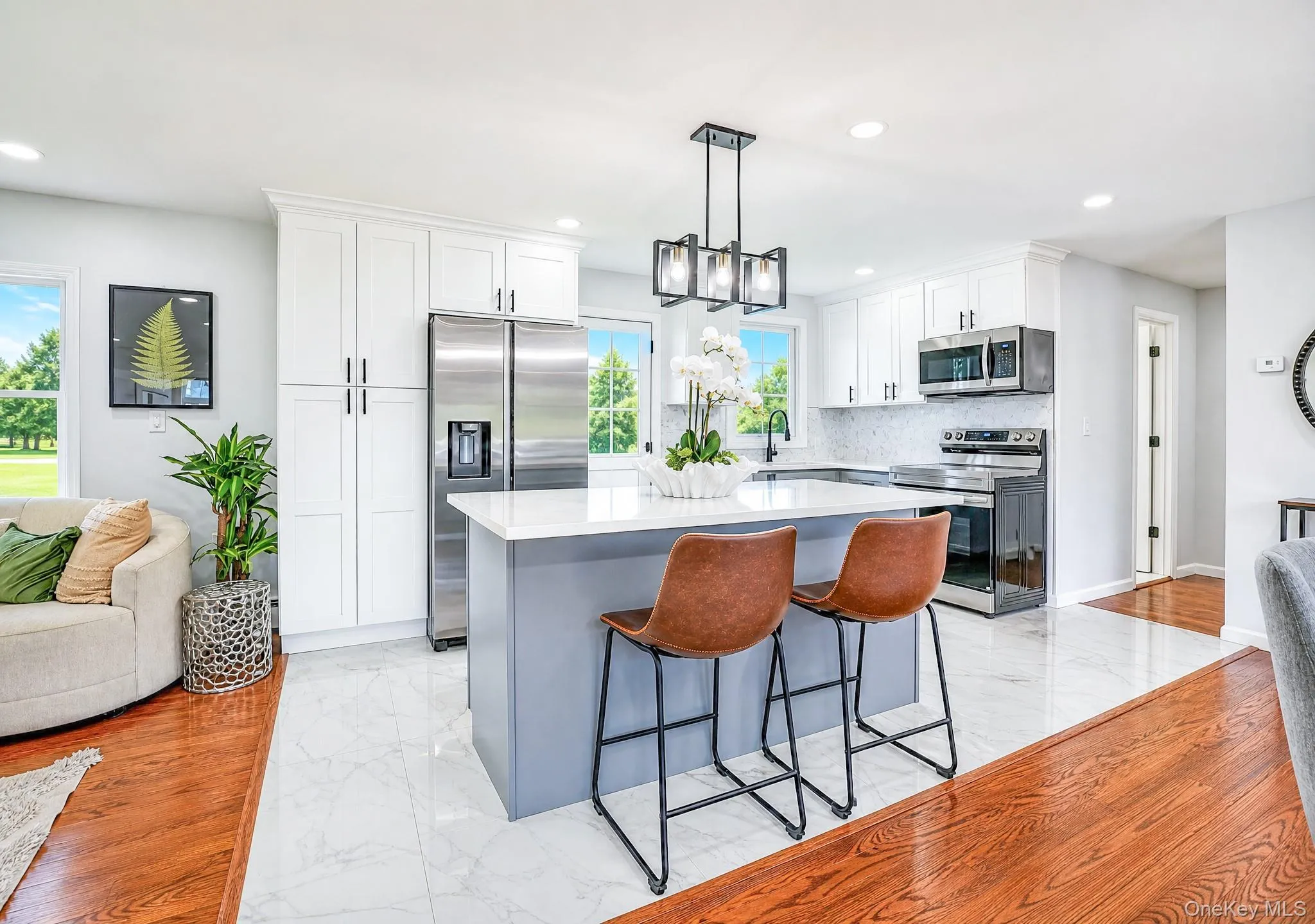 Modern kitchen featuring a central island with a light countertop, white shaker cabinetry, stainless steel appliances, and a mosaic tile backsplash Modern kitchen featuring a central island with a light countertop, white shaker cabinetry, stainless steel appliances, and a mosaic tile backsplash
