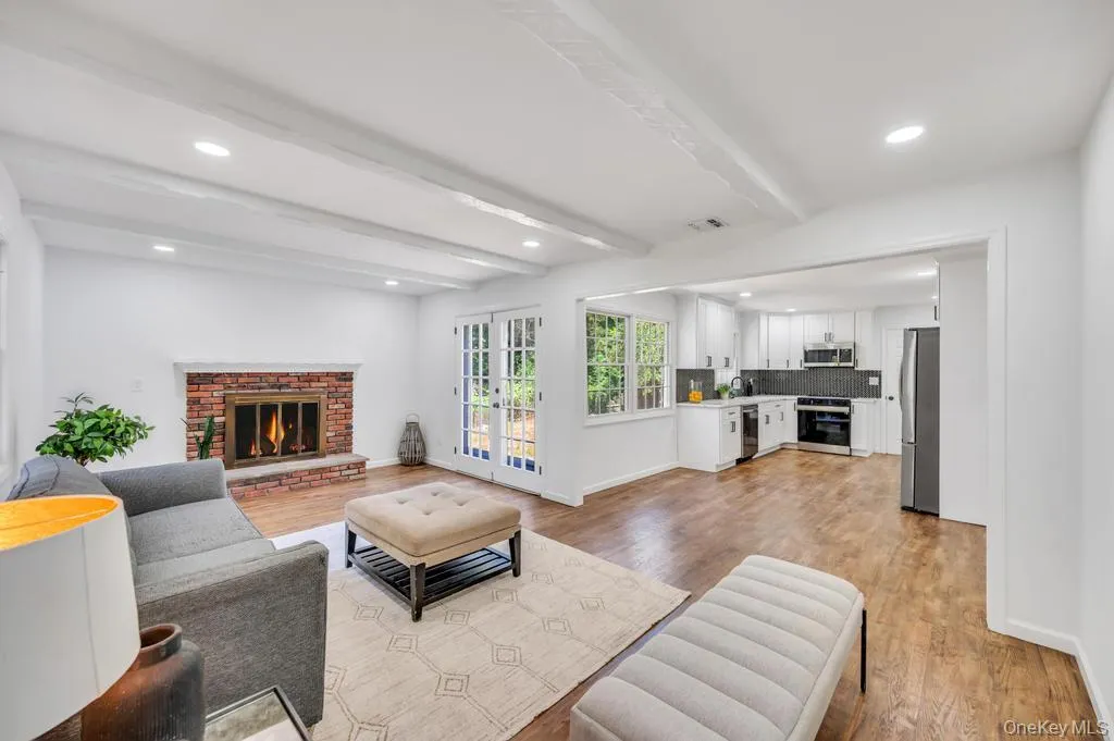 Bright living area featuring a brick fireplace with a white mantel and exposed ceiling beams Bright living area featuring a brick fireplace with a white mantel and exposed ceiling beams