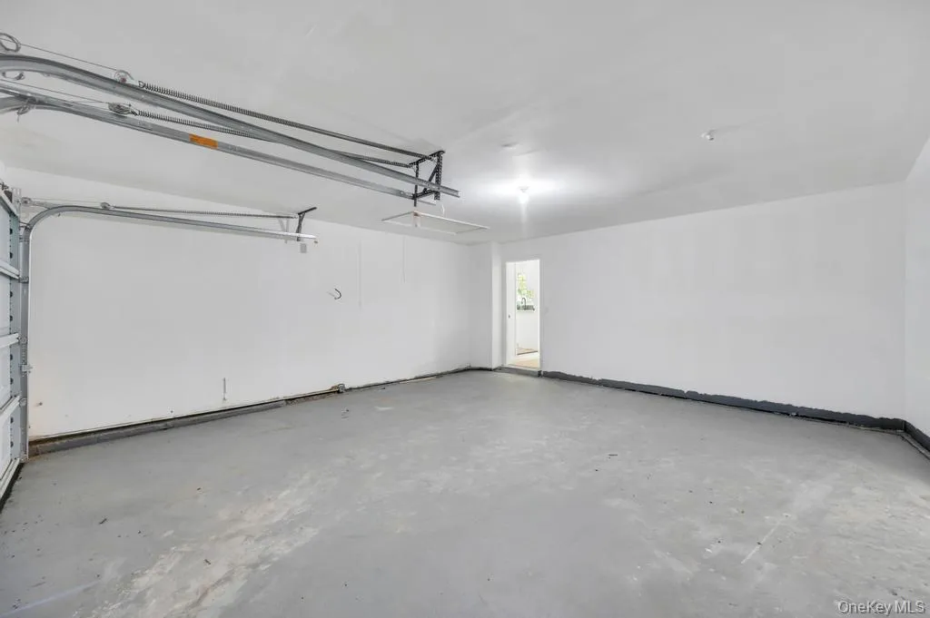 Expansive garage space featuring a concrete floor, white painted walls, overhead lighting, and an overhead door mechanism Expansive garage space featuring a concrete floor, white painted walls, overhead lighting, and an overhead door mechanism