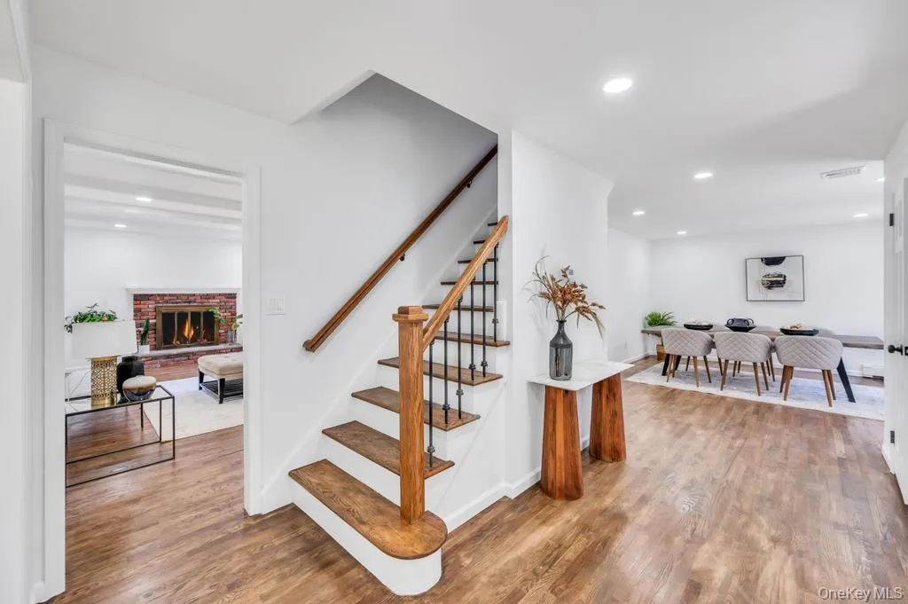 Entryway featuring wood-finish flooring, a staircase with wood treads and wrought iron balusters, an open archway to a dining area with recessed lighting, and a separate doorway to a living space with a brick fireplace Entryway featuring wood-finish flooring, a staircase with wood treads and wrought iron balusters, an open archway to a dining area with recessed lighting, and a separate doorway to a living space with a brick fireplace
