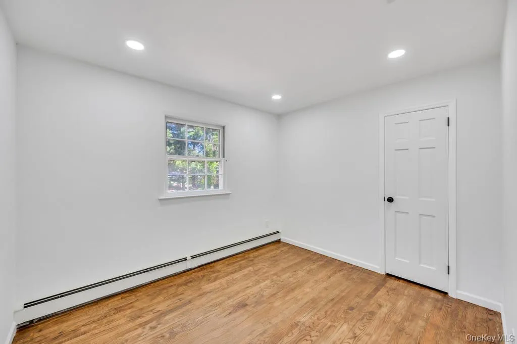 Room featuring wood-finish flooring, recessed lighting, white walls, a six-panel door with a black knob, and a double-hung window Room featuring wood-finish flooring, recessed lighting, white walls, a six-panel door with a black knob, and a double-hung window