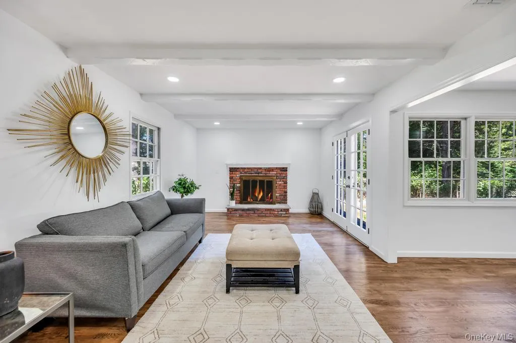 Living area featuring exposed ceiling beams, a brick fireplace, wood-finish flooring, recessed lighting, and white paneled French doors Living area featuring exposed ceiling beams, a brick fireplace, wood-finish flooring, recessed lighting, and white paneled French doors