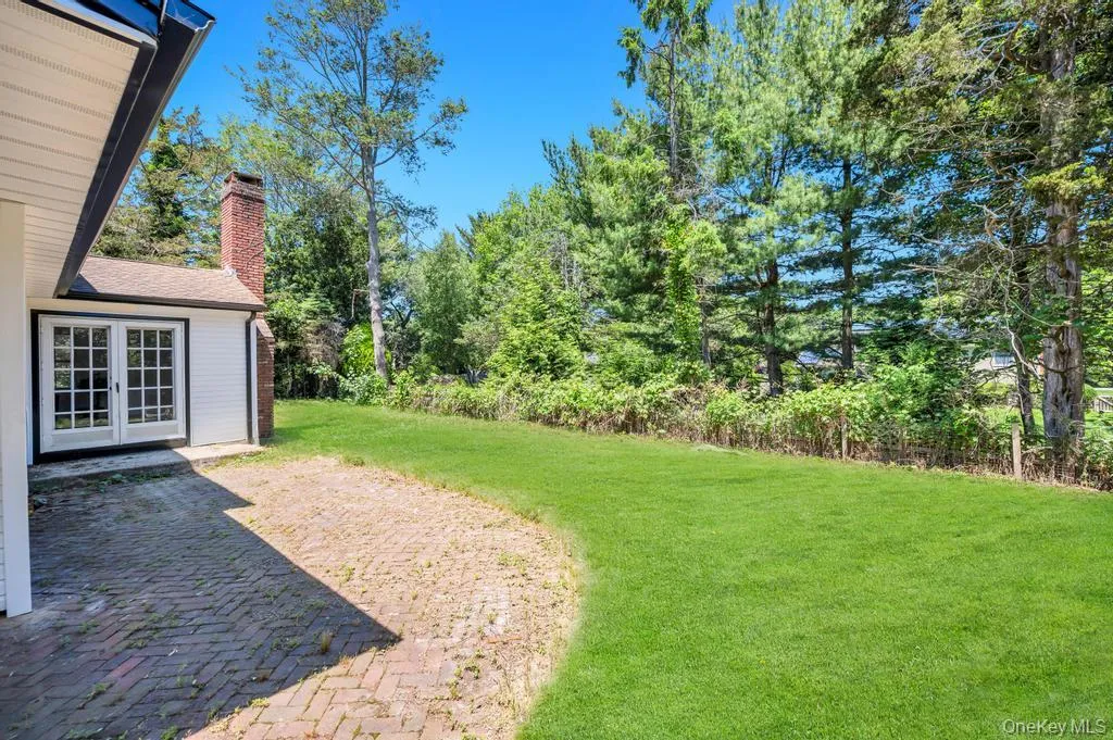 Expansive green lawn framed by mature trees, featuring a brick paver patio and French doors Expansive green lawn framed by mature trees, featuring a brick paver patio and French doors