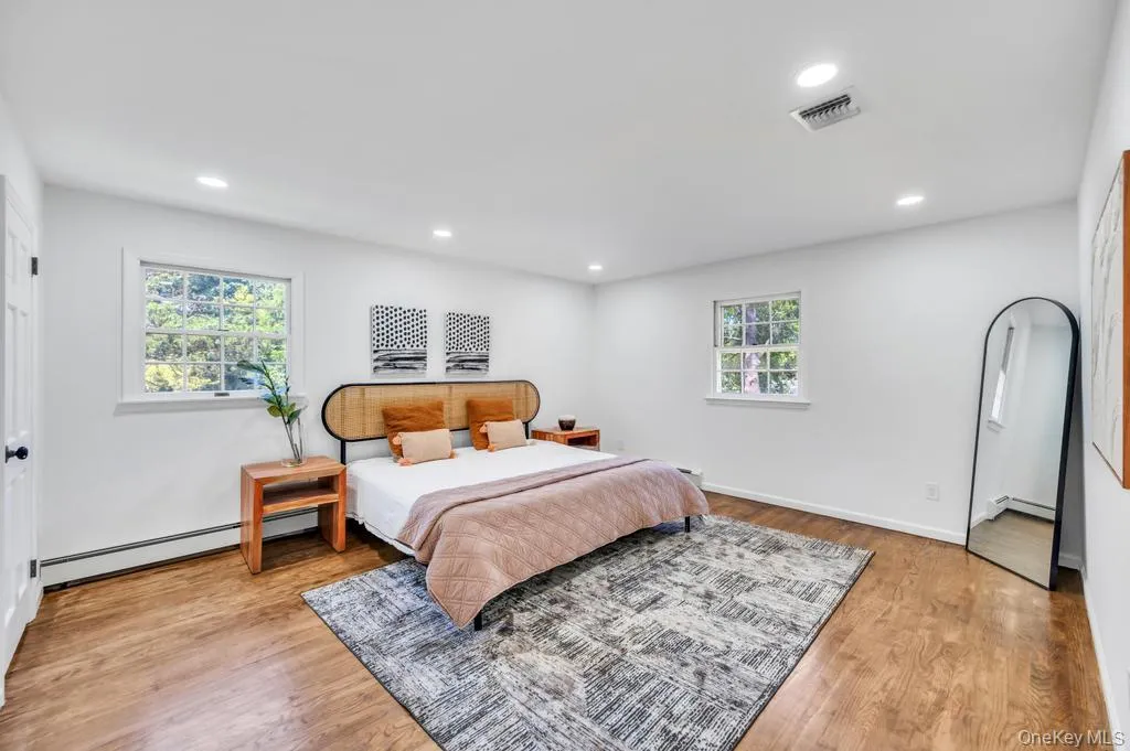 Spacious bedroom featuring wood-finish flooring, recessed lighting, and multiple windows with white trim Spacious bedroom featuring wood-finish flooring, recessed lighting, and multiple windows with white trim