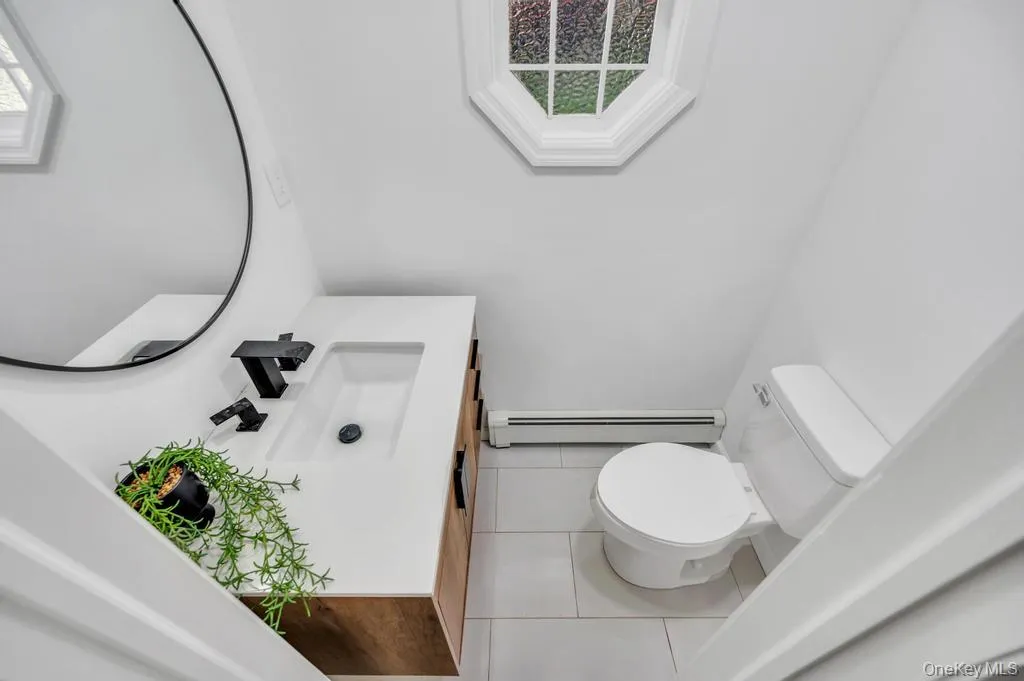 Modern bathroom featuring a wood-finish vanity with a rectangular integrated sink, matte black faucet, and a circular wall mirror Modern bathroom featuring a wood-finish vanity with a rectangular integrated sink, matte black faucet, and a circular wall mirror