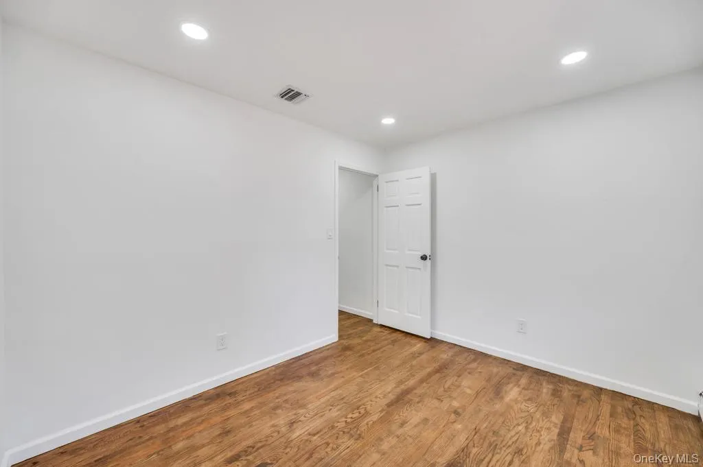 Bright interior space featuring wood-finish flooring, white walls, recessed ceiling lighting, and a paneled door with a black knob Bright interior space featuring wood-finish flooring, white walls, recessed ceiling lighting, and a paneled door with a black knob