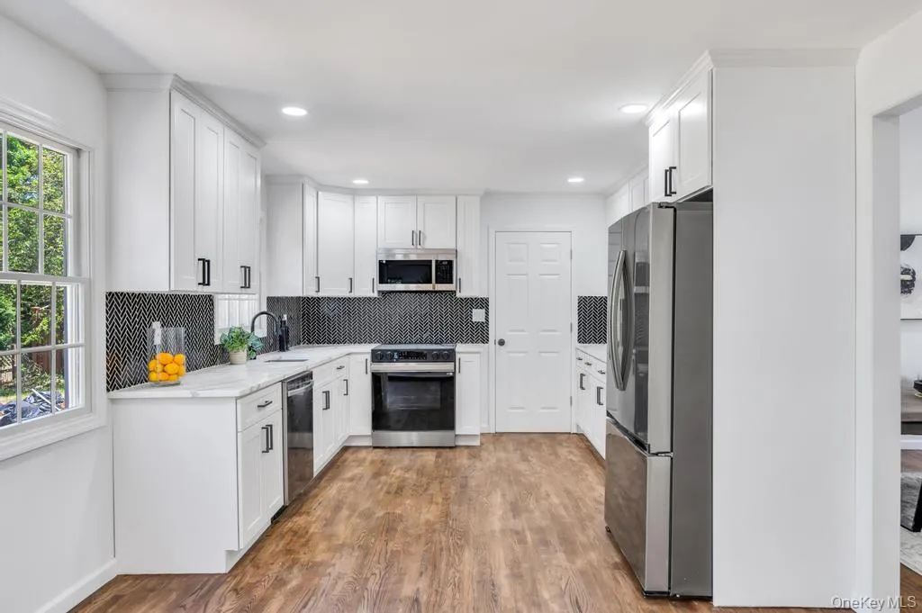 Kitchen featuring white cabinetry, quartz-finish countertops, black herringbone tile backsplash, and wood-finish flooring Kitchen featuring white cabinetry, quartz-finish countertops, black herringbone tile backsplash, and wood-finish flooring