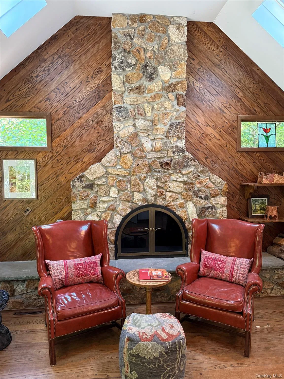 Floor-to-ceiling stone fireplace with an arched firebox, wood-finish flooring, and sloped wood-paneled walls Floor-to-ceiling stone fireplace with an arched firebox, wood-finish flooring, and sloped wood-paneled walls