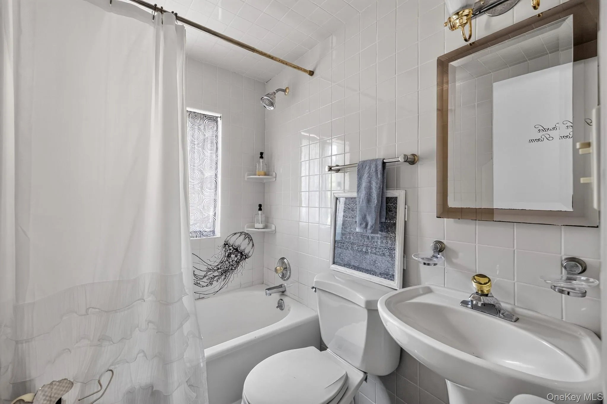 Pedestal sink with chrome and brass-tone faucet, framed wall mirror, and white tiled walls Pedestal sink with chrome and brass-tone faucet, framed wall mirror, and white tiled walls