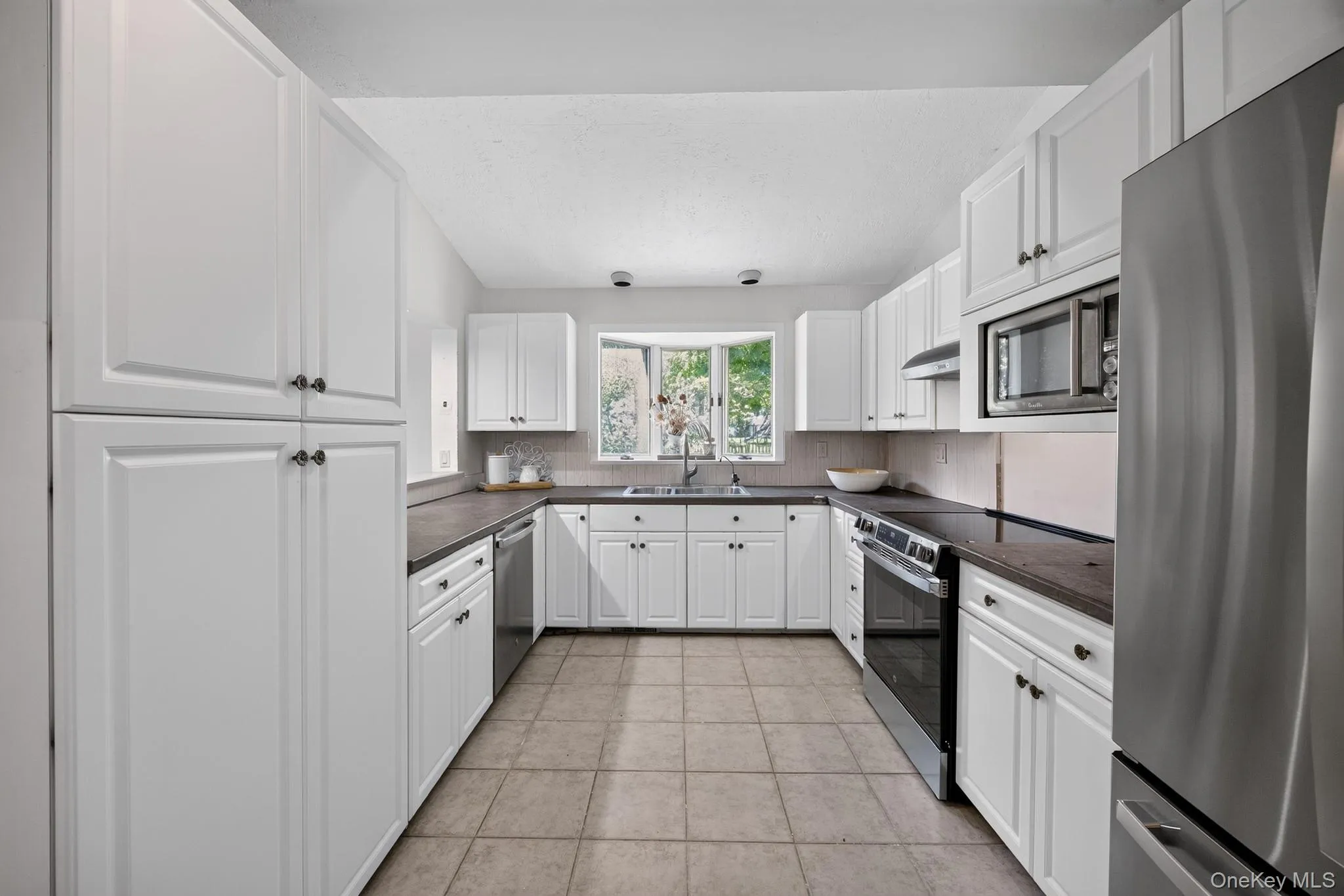 Kitchen featuring white cabinetry, dark countertops, a tile backsplash, and stainless steel appliances Kitchen featuring white cabinetry, dark countertops, a tile backsplash, and stainless steel appliances