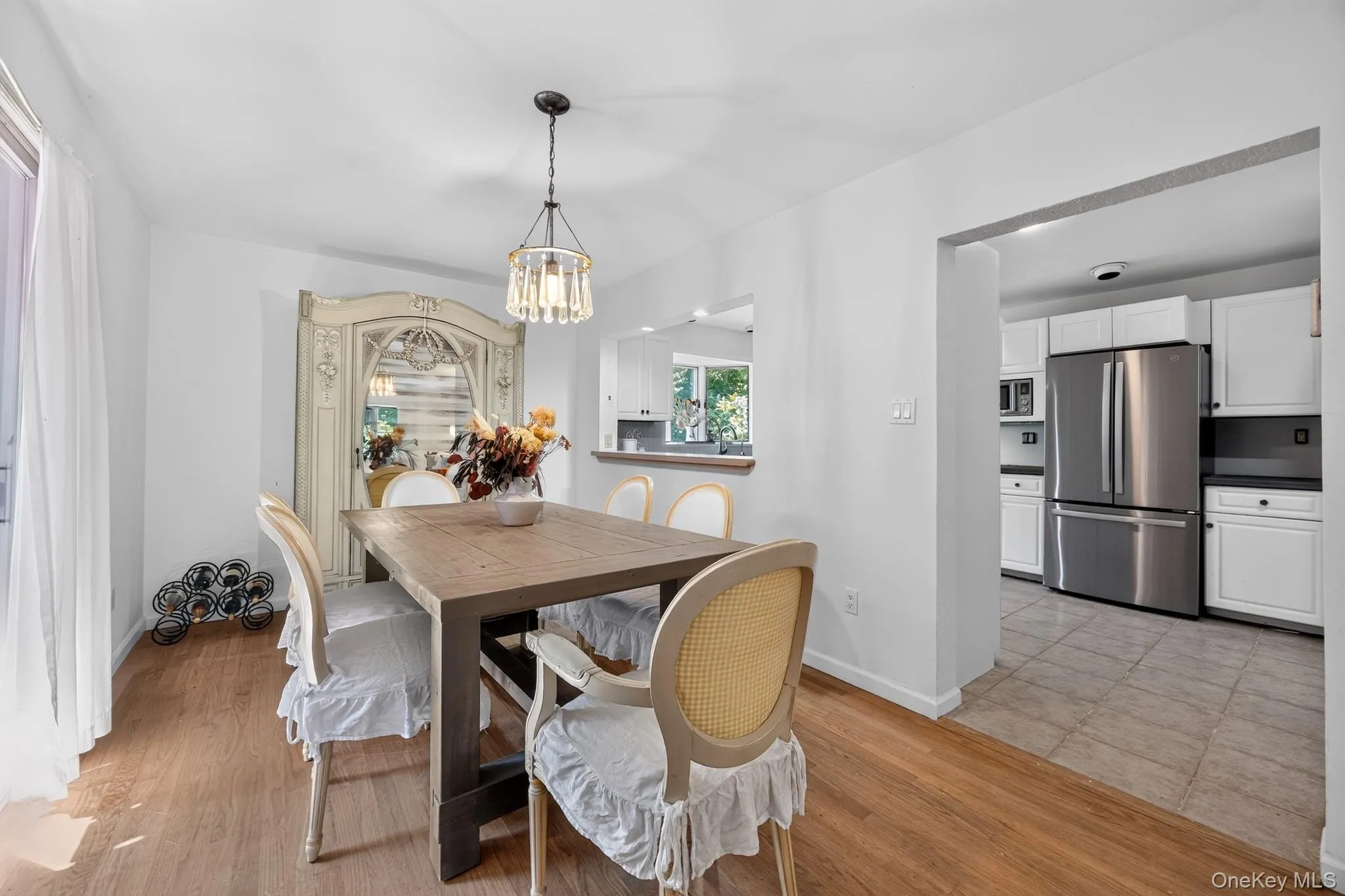 Wood-finish flooring leading to a pass-through kitchen with white cabinetry, stainless steel appliances, and tile flooring Wood-finish flooring leading to a pass-through kitchen with white cabinetry, stainless steel appliances, and tile flooring