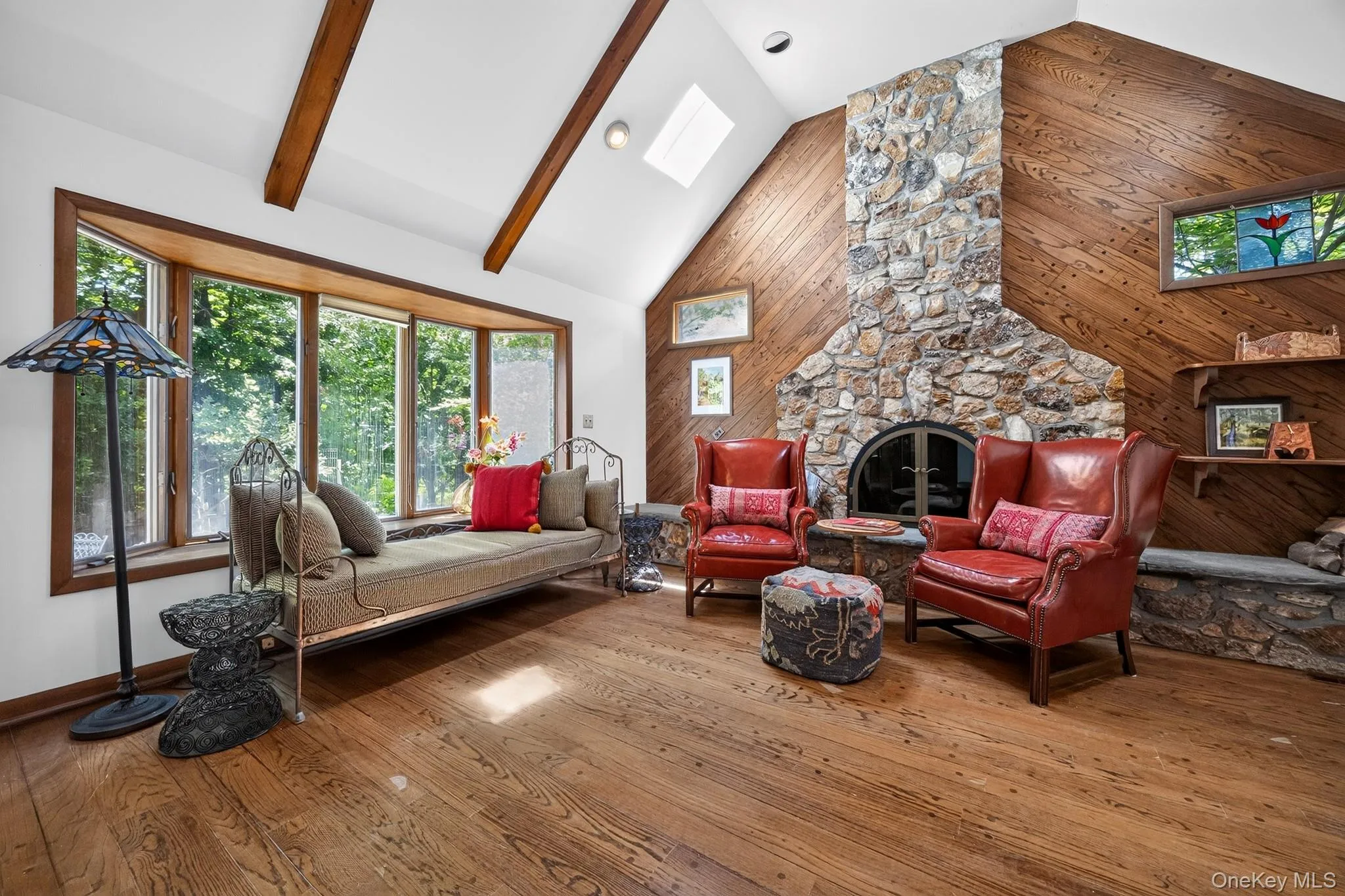 Vaulted ceiling with exposed wood beams, stone-clad fireplace, rich wood-finish flooring, bay window, and skylight Vaulted ceiling with exposed wood beams, stone-clad fireplace, rich wood-finish flooring, bay window, and skylight