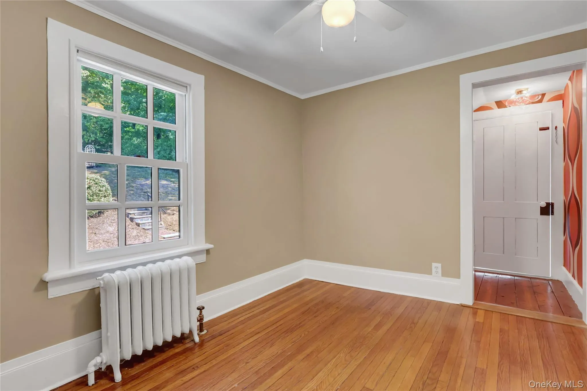 Unfurnished room featuring radiator, light wood finished floors, ornamental molding, and ceiling fan Unfurnished room featuring radiator, light wood finished floors, ornamental molding, and ceiling fan