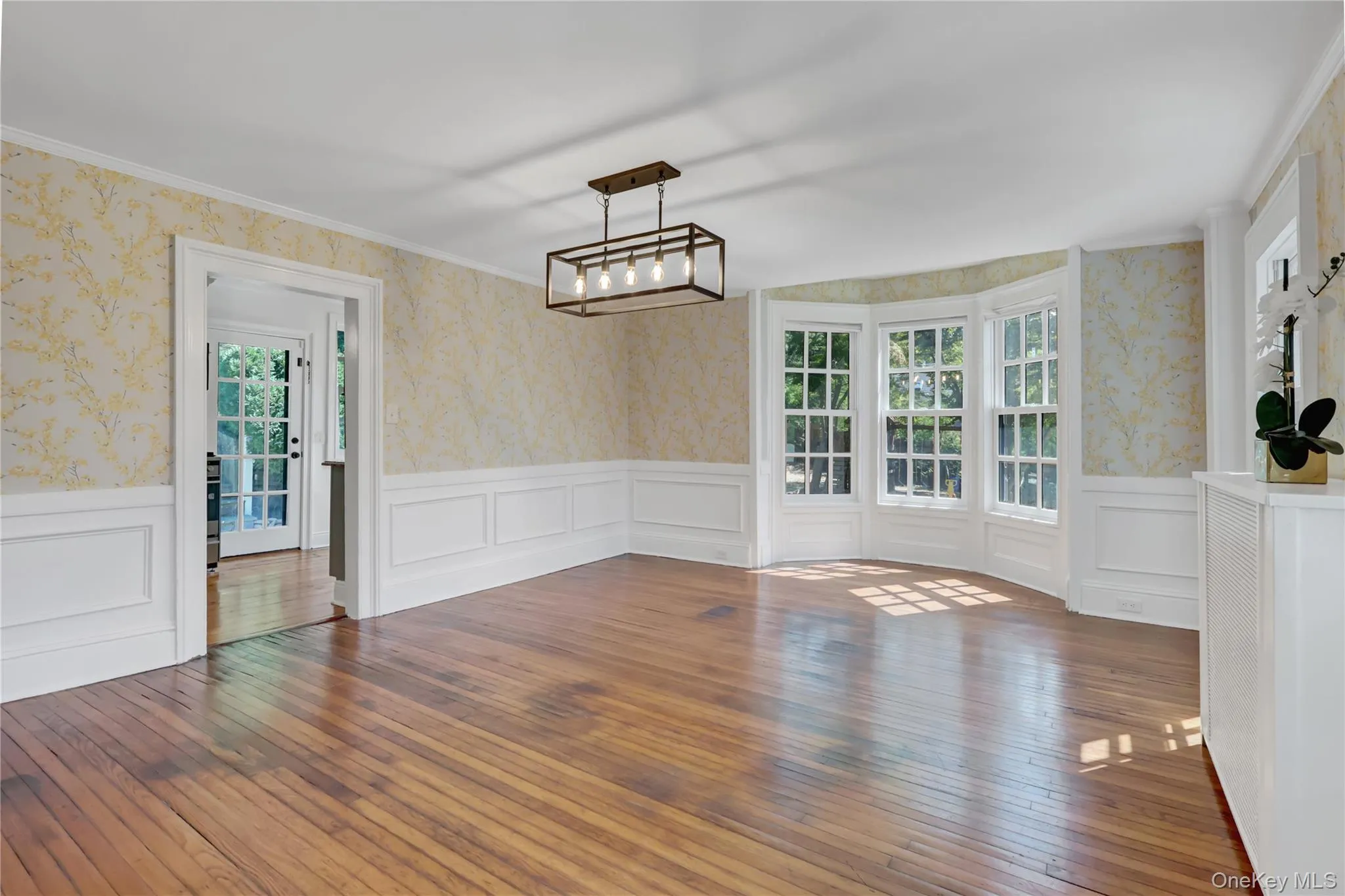Unfurnished dining area with wallpapered walls, plenty of natural light, dark wood-style flooring, ornamental molding, and a wainscoted wall Unfurnished dining area with wallpapered walls, plenty of natural light, dark wood-style flooring, ornamental molding, and a wainscoted wall