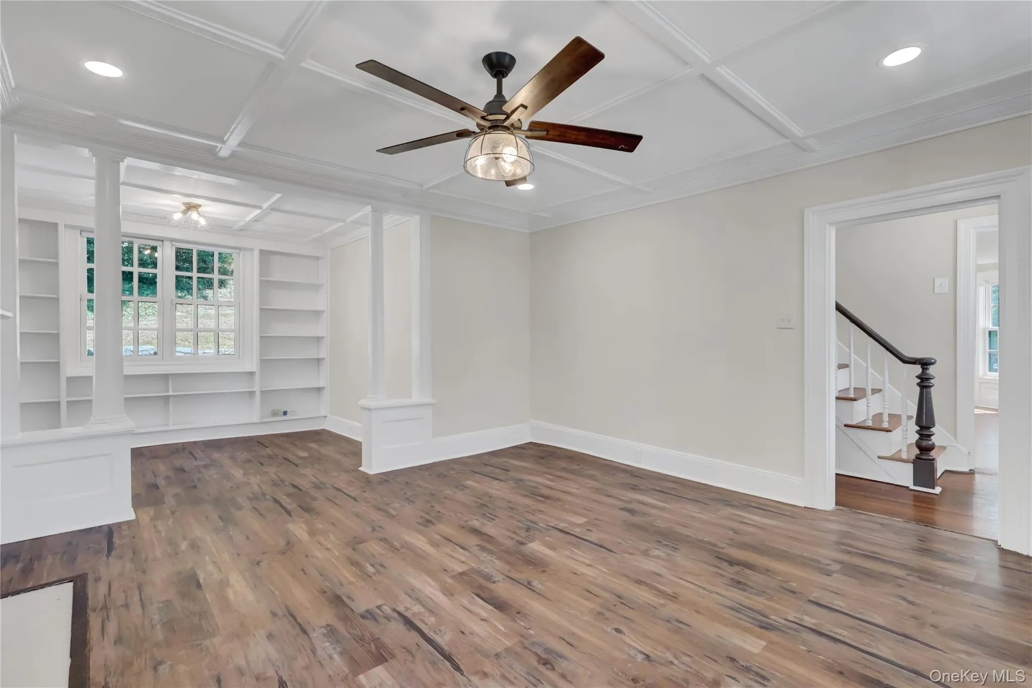 Unfurnished room with built in shelves, stairs, a ceiling fan, dark wood-style floors, and recessed lighting Unfurnished room with built in shelves, stairs, a ceiling fan, dark wood-style floors, and recessed lighting