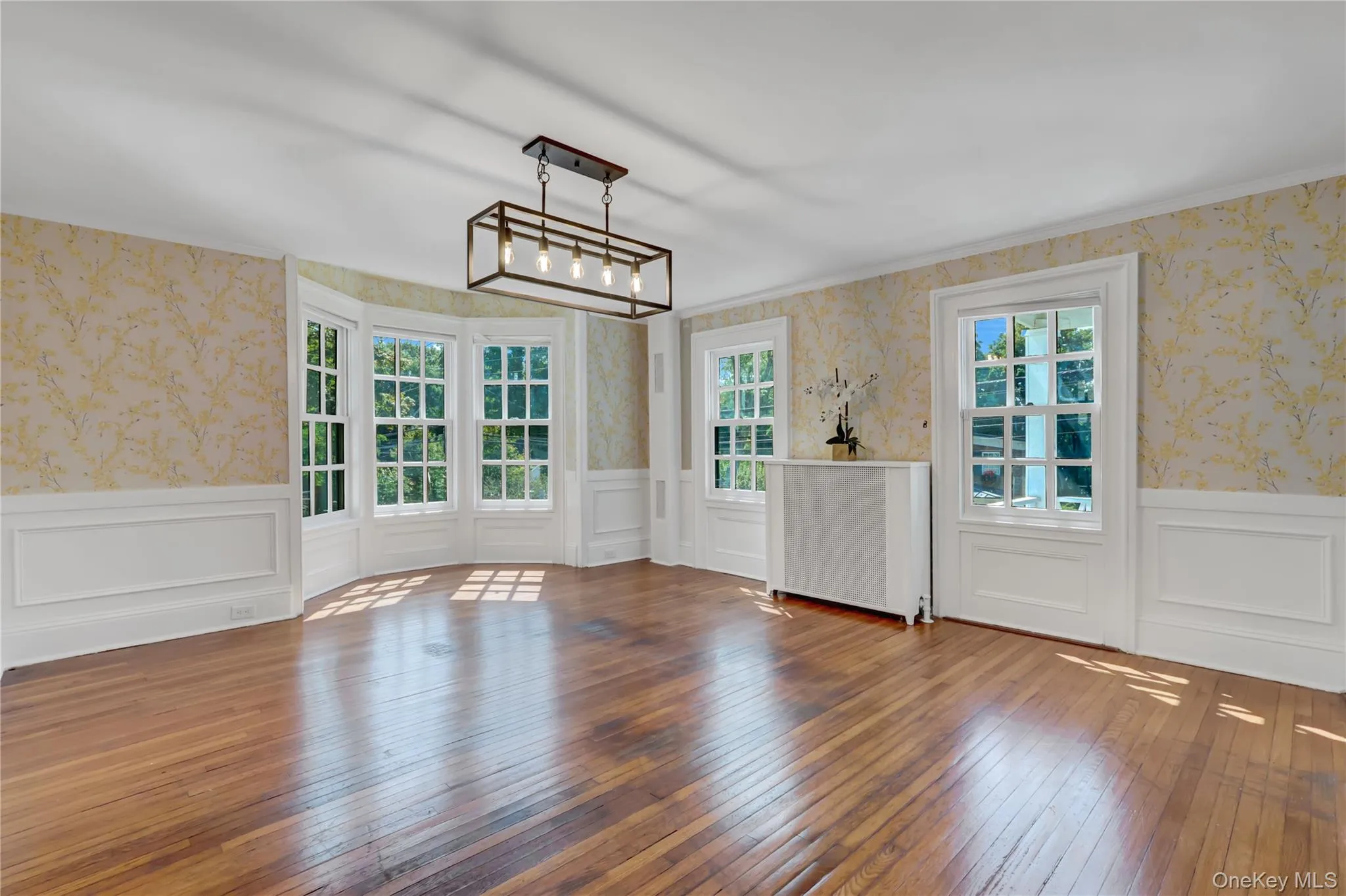 Unfurnished dining area featuring wallpapered walls, wood-type flooring, a wainscoted wall, and a decorative wall Unfurnished dining area featuring wallpapered walls, wood-type flooring, a wainscoted wall, and a decorative wall