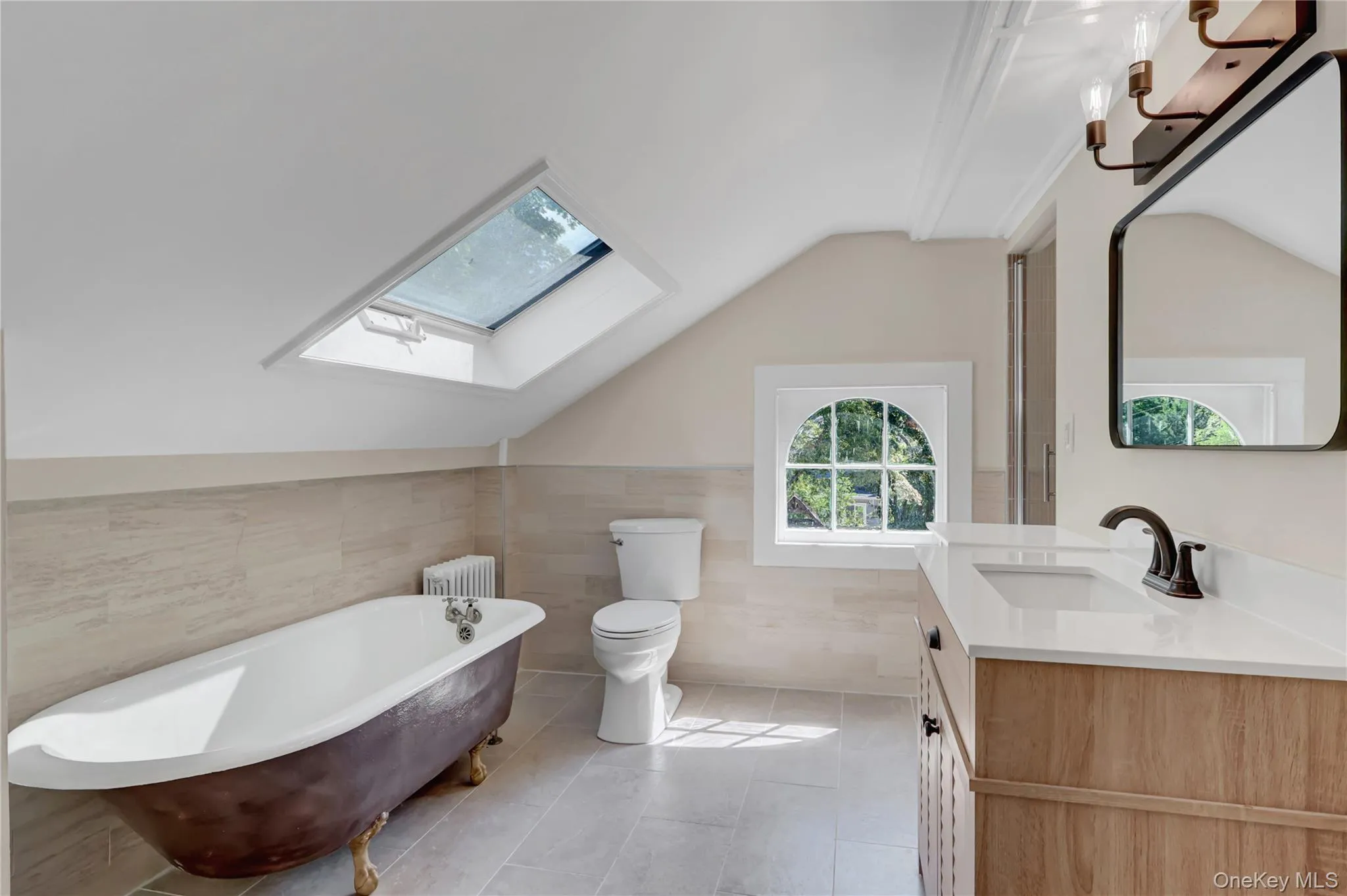 Full bath with vaulted ceiling, tile walls, a freestanding bath, vanity, and light tile patterned flooring Full bath with vaulted ceiling, tile walls, a freestanding bath, vanity, and light tile patterned flooring