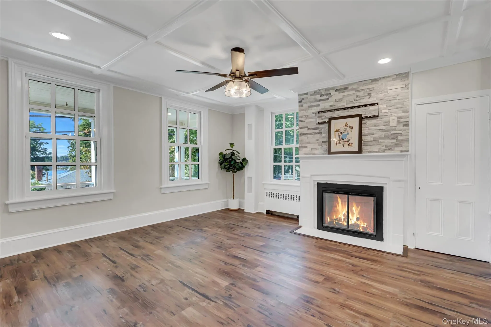 Unfurnished living room with a large fireplace, coffered ceiling, wood finished floors, radiator, and ceiling fan Unfurnished living room with a large fireplace, coffered ceiling, wood finished floors, radiator, and ceiling fan