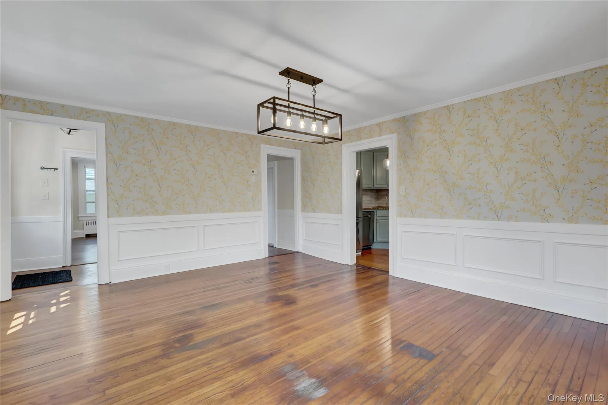 Unfurnished room featuring wallpapered walls, hardwood / wood-style flooring, wainscoting, radiator heating unit, and ornamental molding Unfurnished room featuring wallpapered walls, hardwood / wood-style flooring, wainscoting, radiator heating unit, and ornamental molding