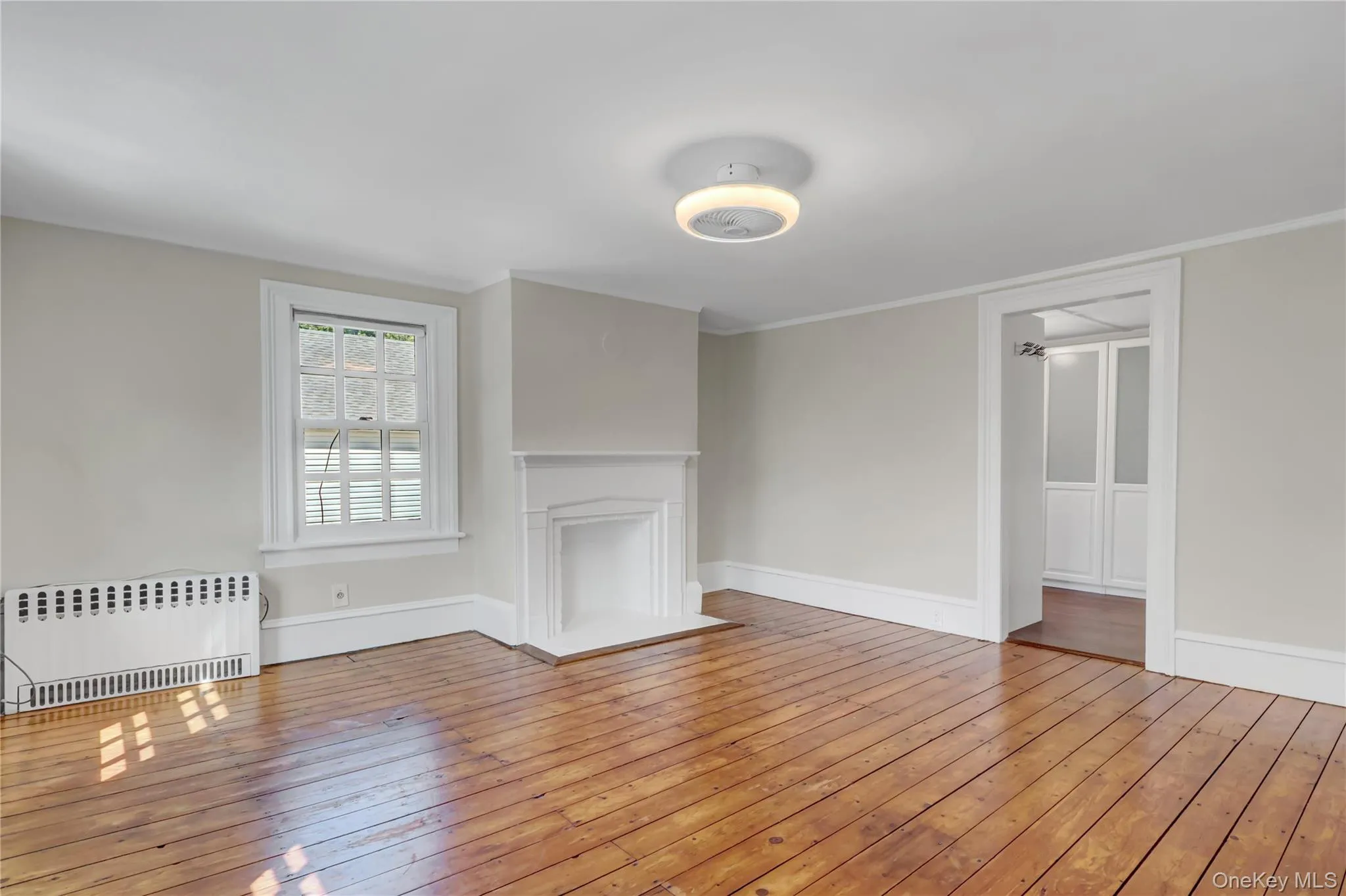 Unfurnished living room featuring radiator heating unit, light wood-type flooring, and ornamental molding Unfurnished living room featuring radiator heating unit, light wood-type flooring, and ornamental molding