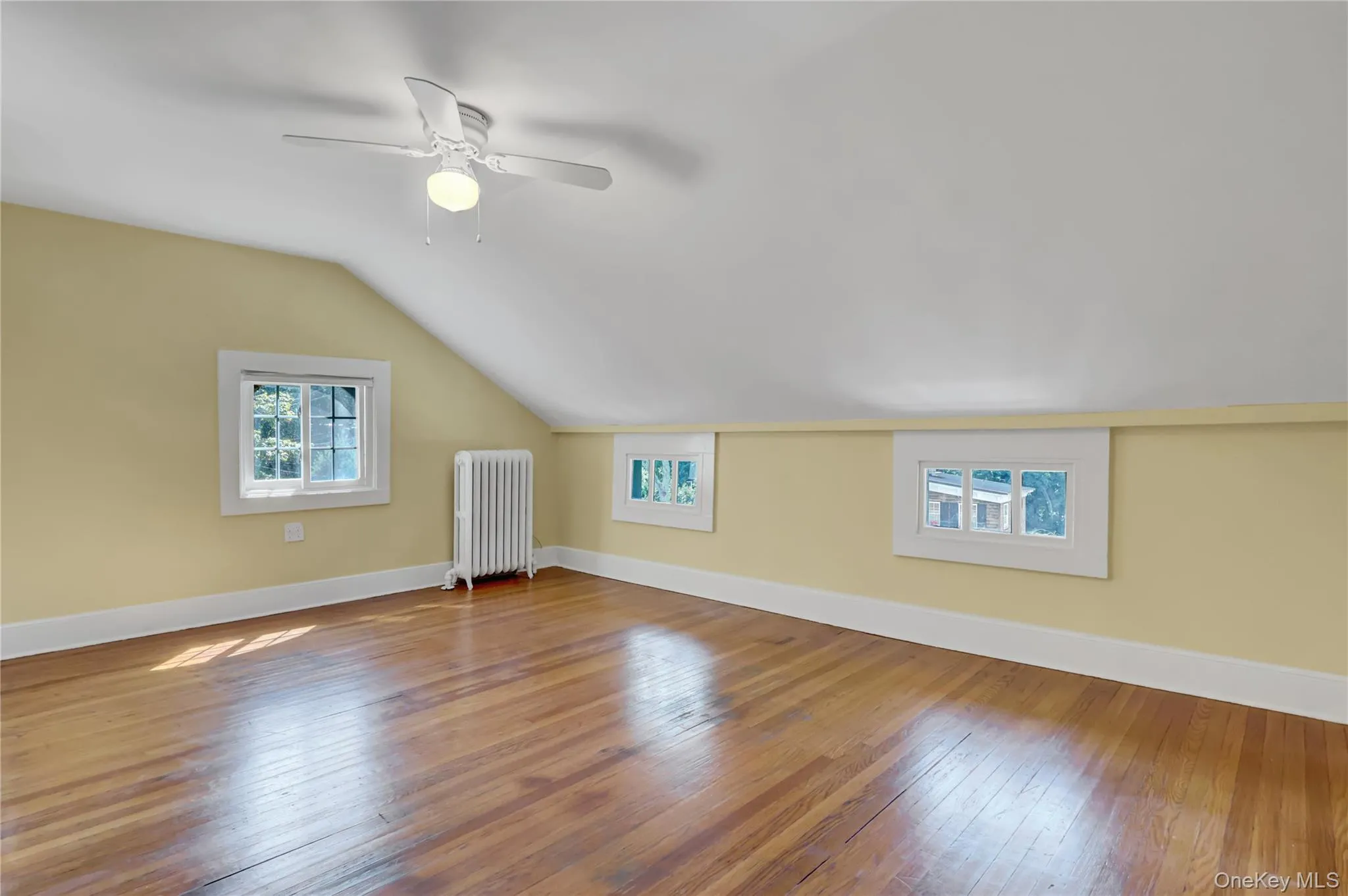 Additional living space with lofted ceiling, radiator heating unit, hardwood / wood-style floors, and ceiling fan Additional living space with lofted ceiling, radiator heating unit, hardwood / wood-style floors, and ceiling fan