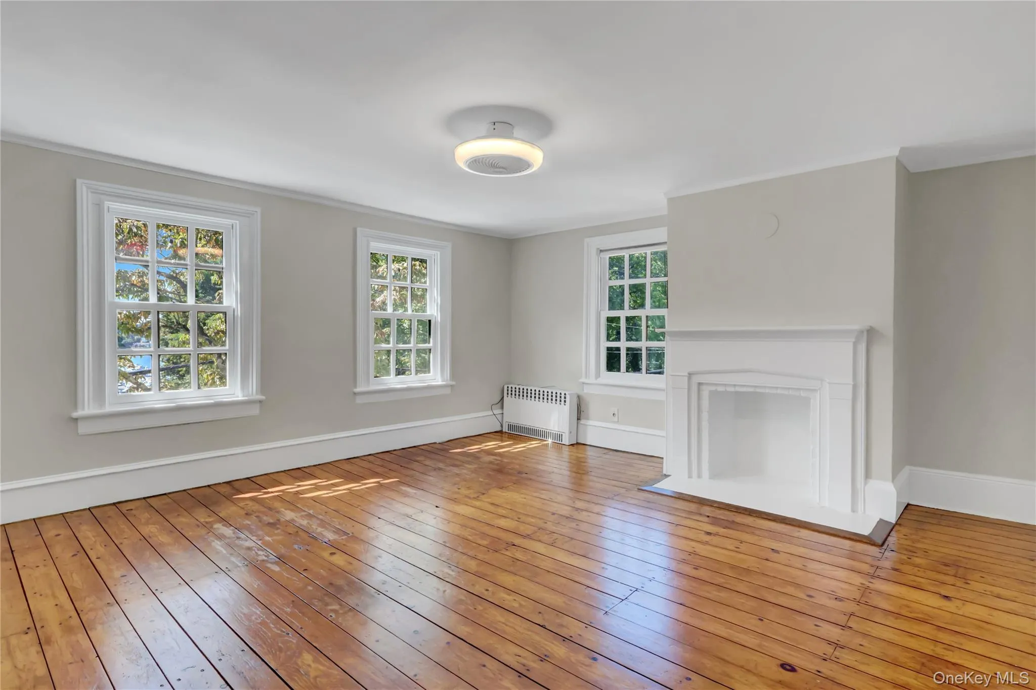 Unfurnished living room with hardwood / wood-style floors, radiator, ornamental molding, and a fireplace with flush hearth Unfurnished living room with hardwood / wood-style floors, radiator, ornamental molding, and a fireplace with flush hearth