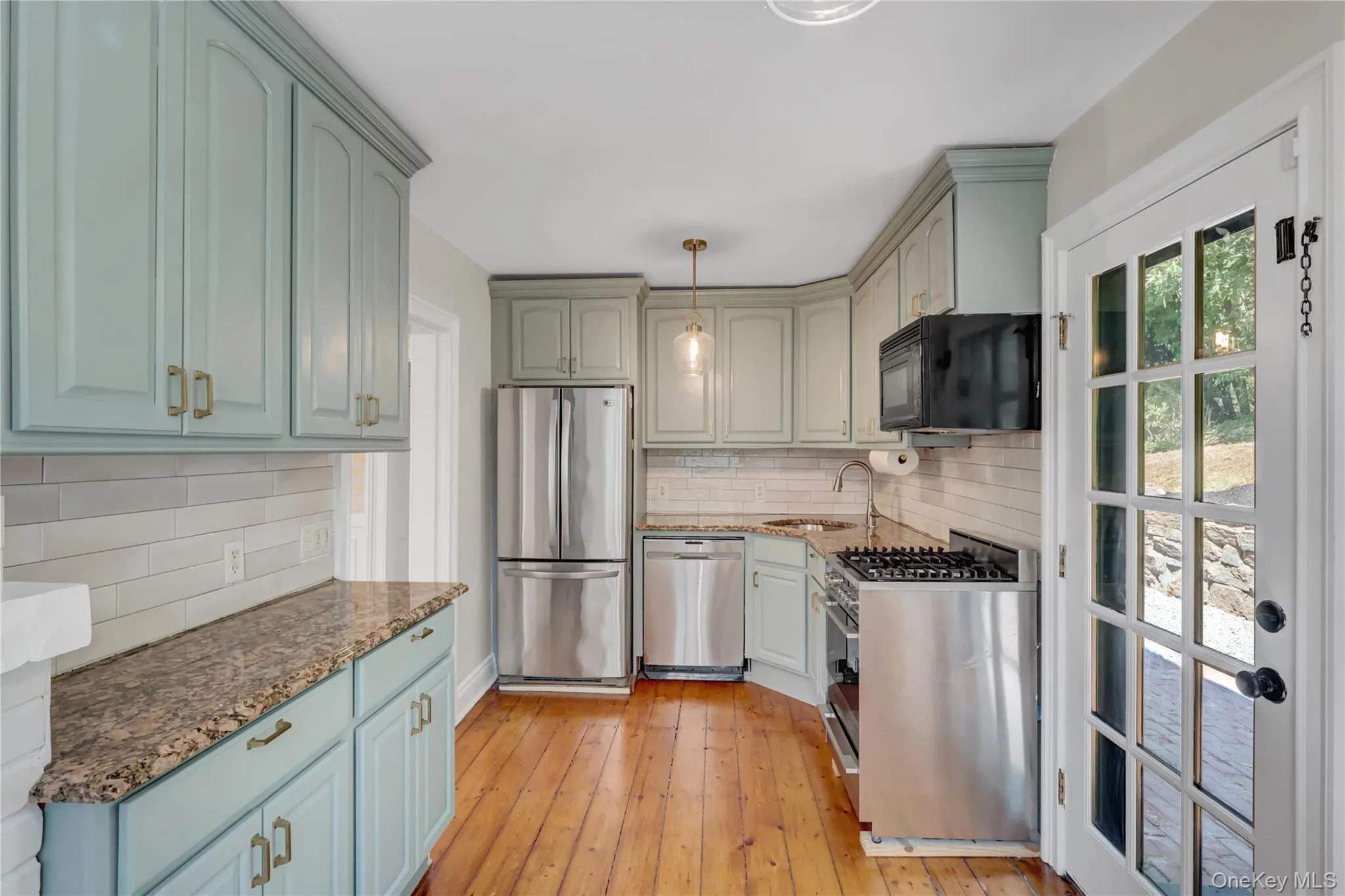 Kitchen featuring stainless steel appliances, dark stone counters, pendant lighting, light wood-style flooring, and decorative backsplash Kitchen featuring stainless steel appliances, dark stone counters, pendant lighting, light wood-style flooring, and decorative backsplash