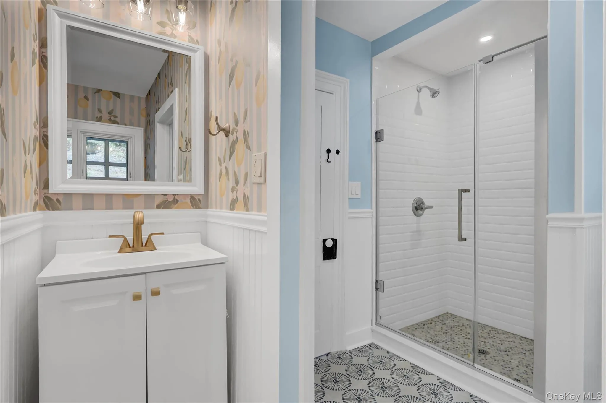 Full bathroom with a shower stall, vanity, wallpapered walls, and a wainscoted wall Full bathroom with a shower stall, vanity, wallpapered walls, and a wainscoted wall