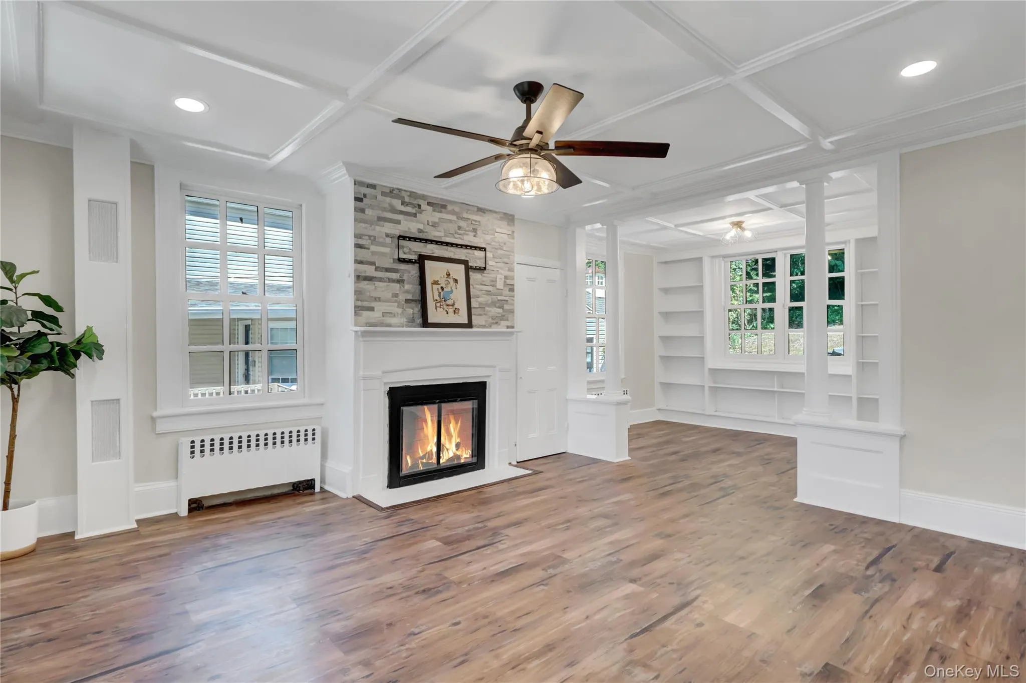 Unfurnished living room featuring built in features, radiator, coffered ceiling, ceiling fan, and wood finished floors Unfurnished living room featuring built in features, radiator, coffered ceiling, ceiling fan, and wood finished floors