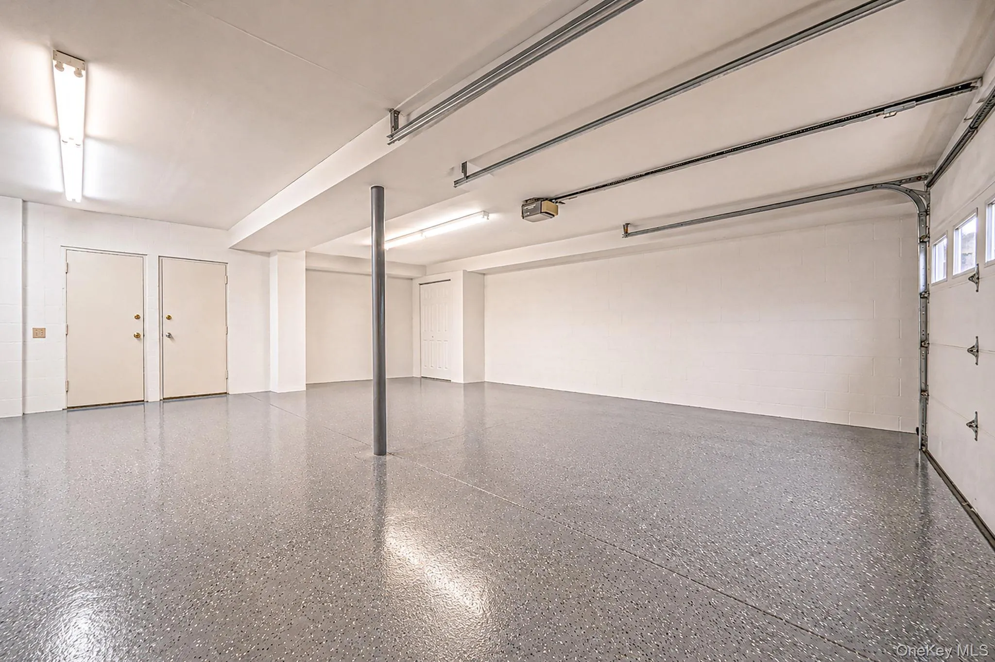 Epoxy-coated flooring, white walls, overhead fluorescent lighting, two panel doors, and a roll-up garage door with windows Epoxy-coated flooring, white walls, overhead fluorescent lighting, two panel doors, and a roll-up garage door with windows