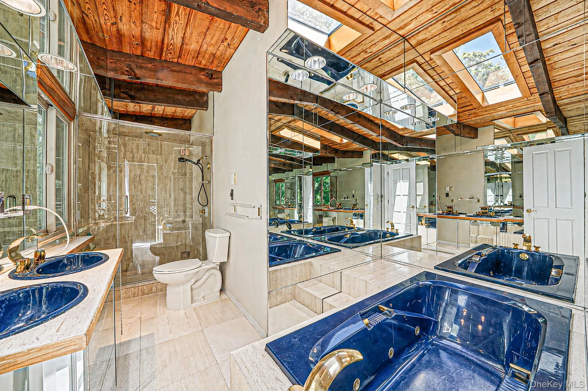 Wood-beamed vaulted ceiling with skylights, mirrored walls, dual integrated deep blue sinks, a walk-in shower with glass enclosure, and a built-in jetted tub Wood-beamed vaulted ceiling with skylights, mirrored walls, dual integrated deep blue sinks, a walk-in shower with glass enclosure, and a built-in jetted tub