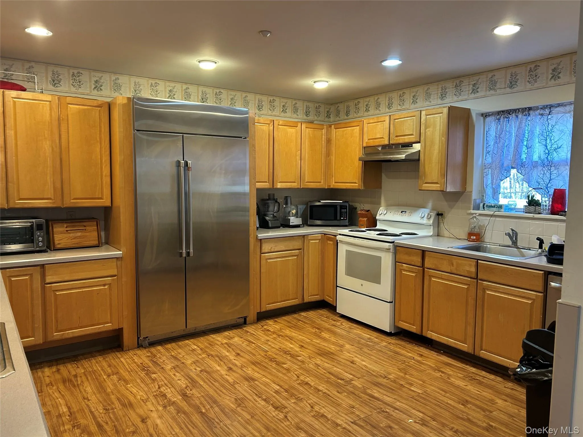 Kitchen with stainless steel appliances, light countertops, light wood-style flooring, under cabinet range hood, and backsplash Kitchen with stainless steel appliances, light countertops, light wood-style flooring, under cabinet range hood, and backsplash